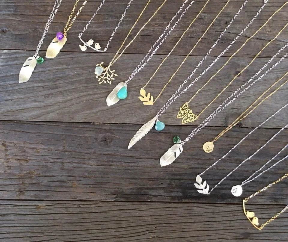 Collection of gold and silver necklaces with various charms and pendants displayed on a wooden surface.