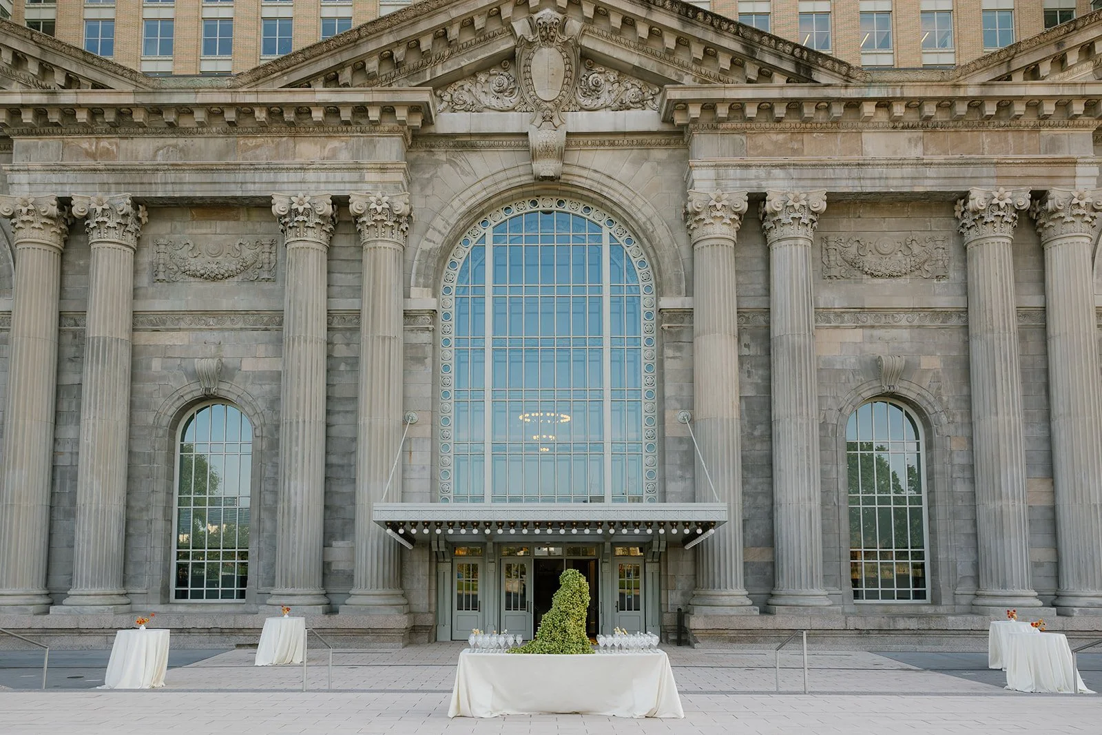 Neoclassical building facade with ornate columns, arched windows, and outdoor event tables.