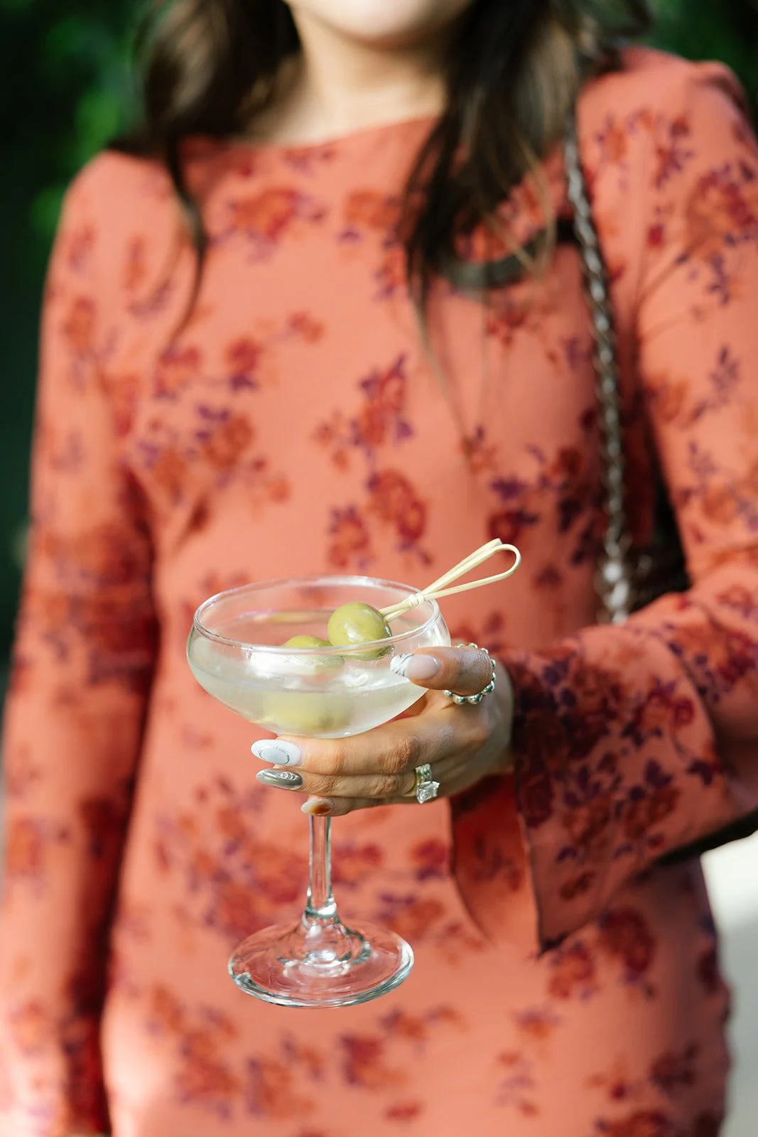 Woman in a coral floral dress holding a coupe glass cocktail garnished with green grapes