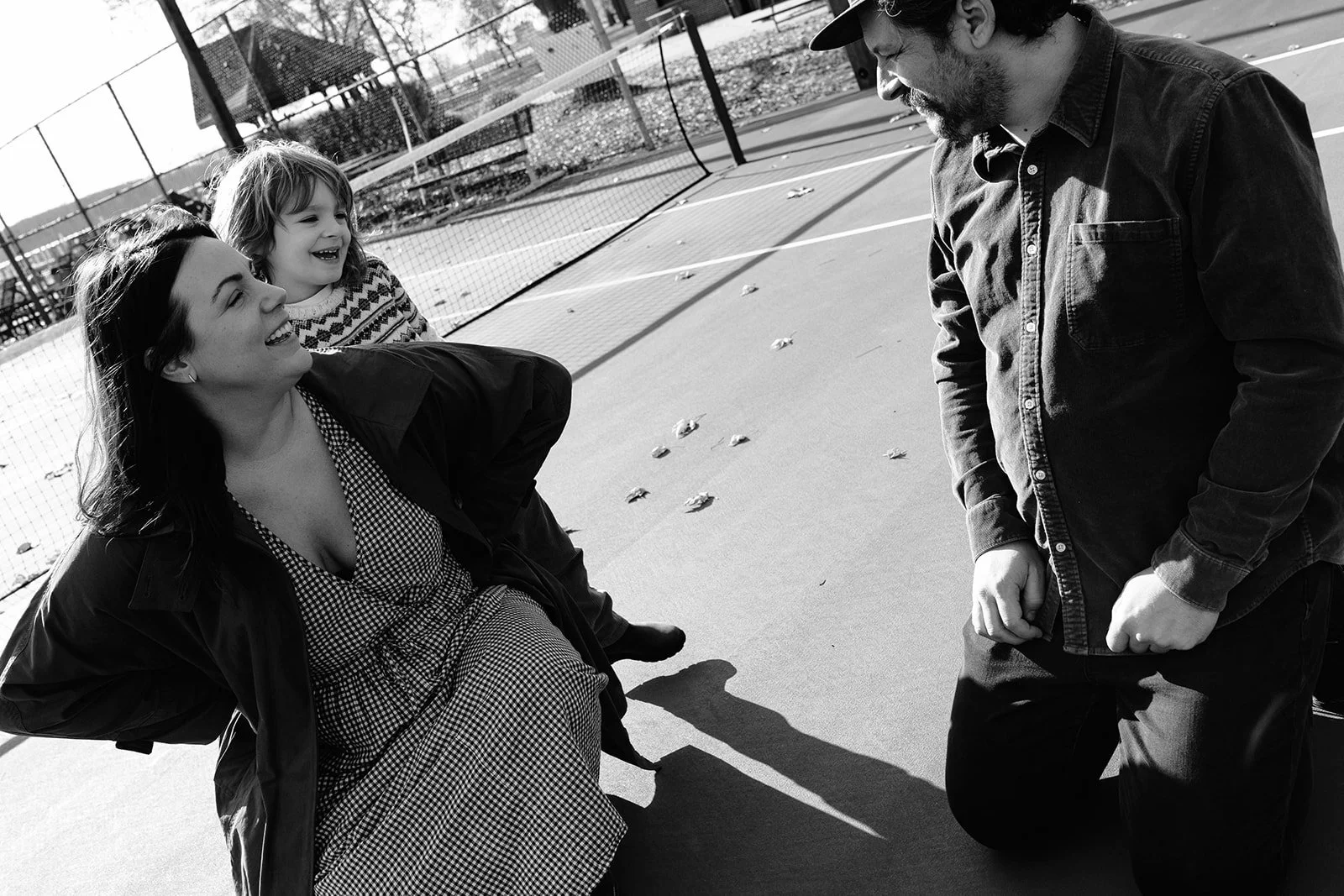 Black-and-white photo of a smiling family talking on an outdoor pickleball court.