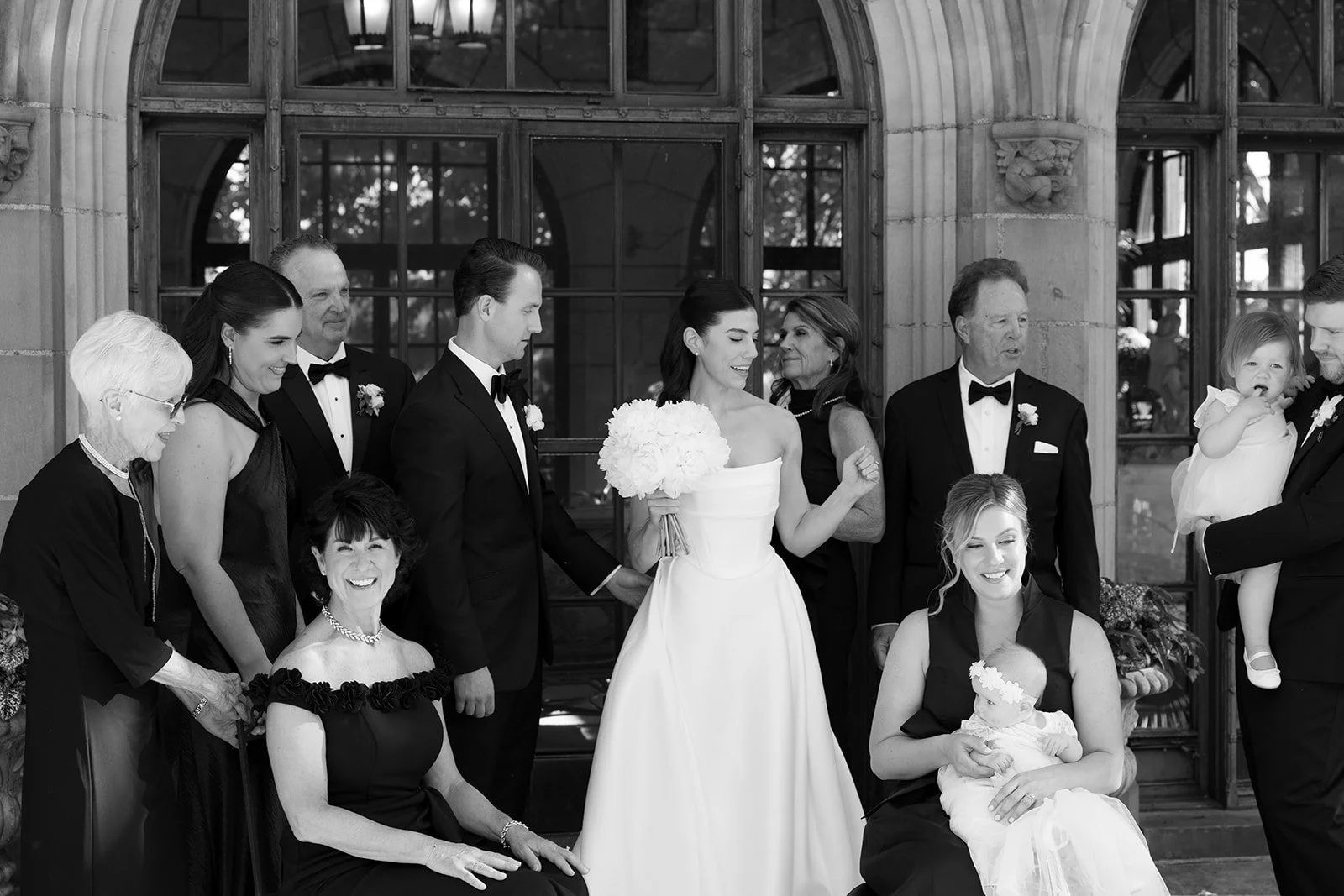 Black-and-white wedding portrait of a bride, groom, and family members outside a grand arched doorway