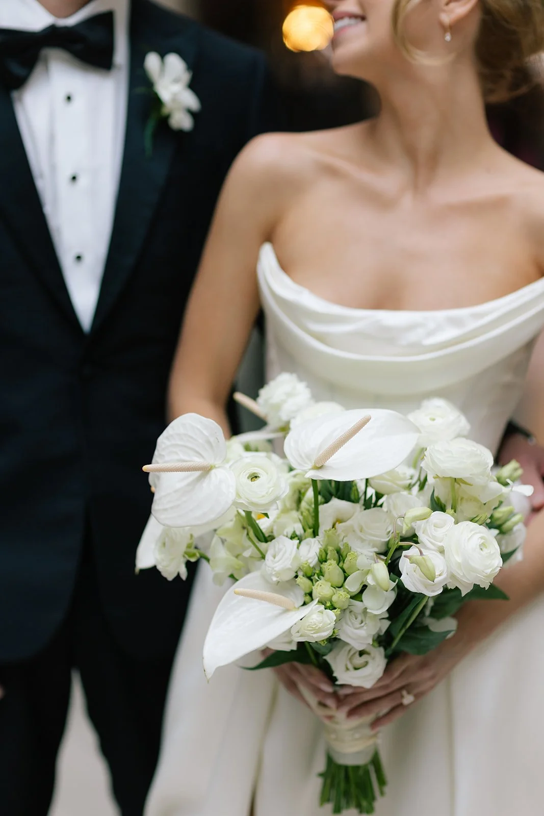 Bride in a white wedding dress holding a white floral bouquet beside a groom in a black tuxedo