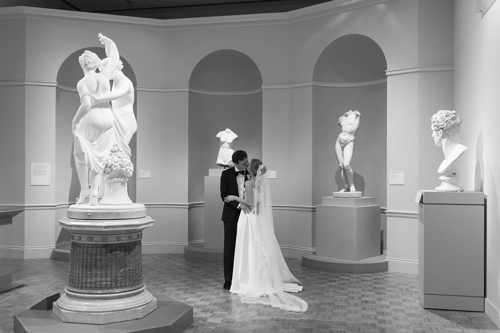 Bride and groom embracing among classical marble sculptures in a museum gallery