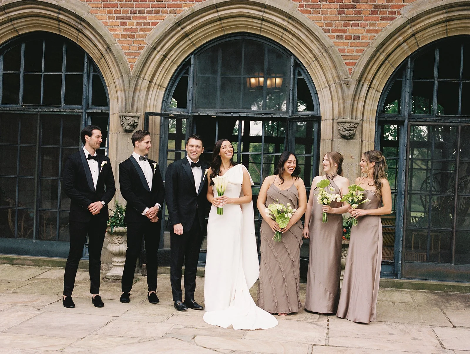 Bride and groom with bridesmaids and groomsmen posing outside a historic brick building
