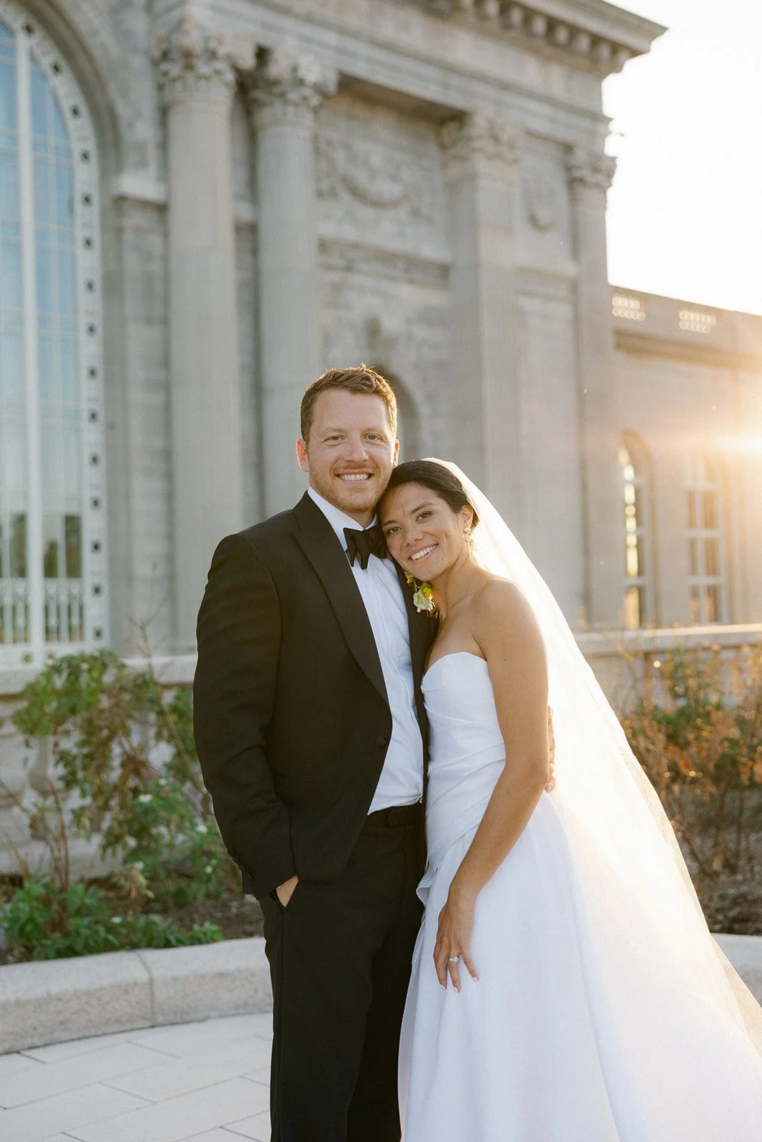 Newlywed couple posing outside a grand classical building at sunset