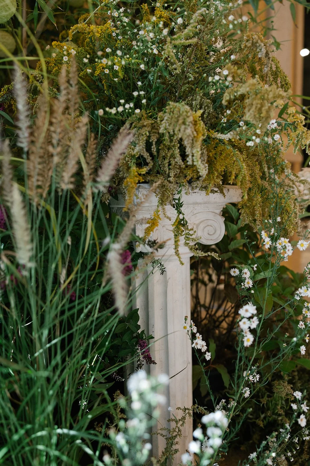 Lush wildflower arrangement in an ornate white classical column planter