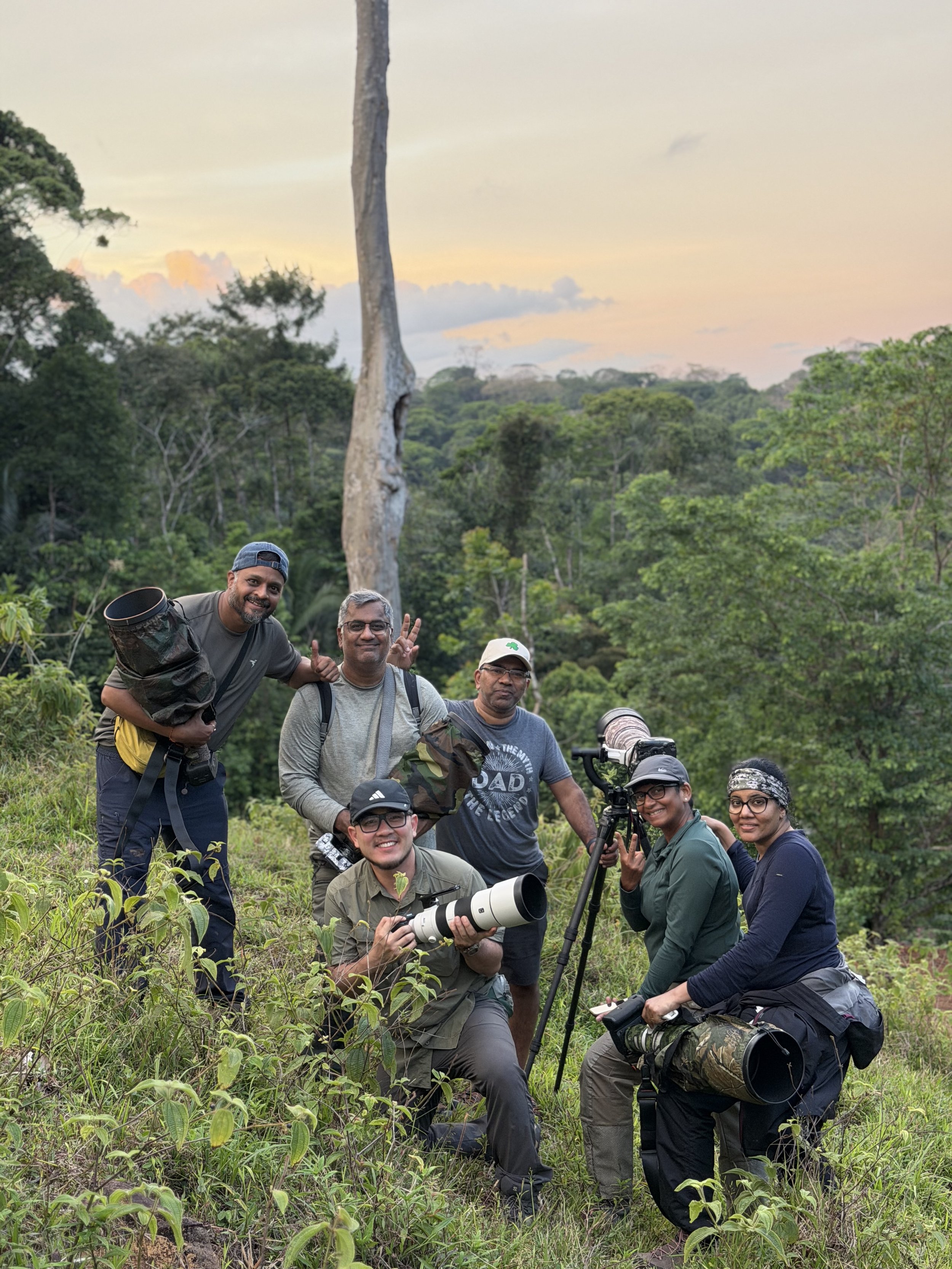 Group of wildlife photographers posing with telephoto cameras in a lush forest at sunset