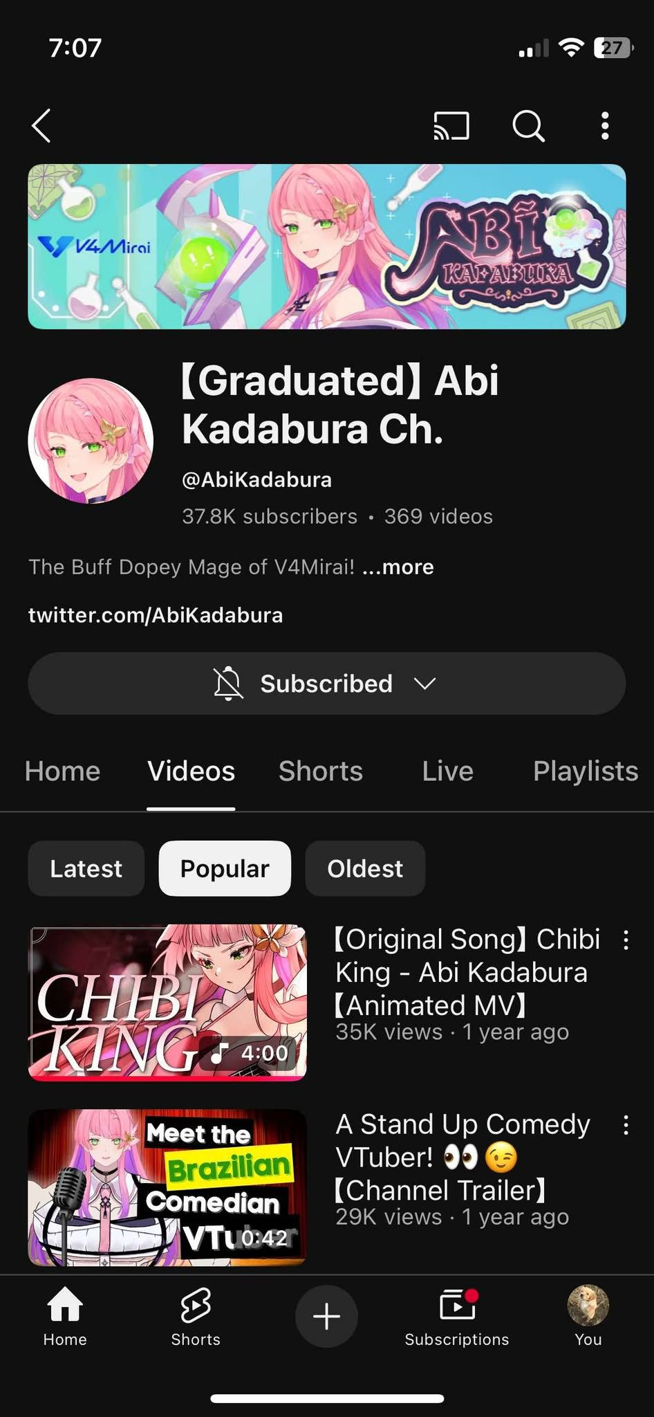 YouTube profile page of Abi Kadabura, a VTuber with a pink/blue hair character icon, featuring a banner promoting her channel, which includes various animated illustrations, with a favorite character, a pink-haired girl, in multiple videos.