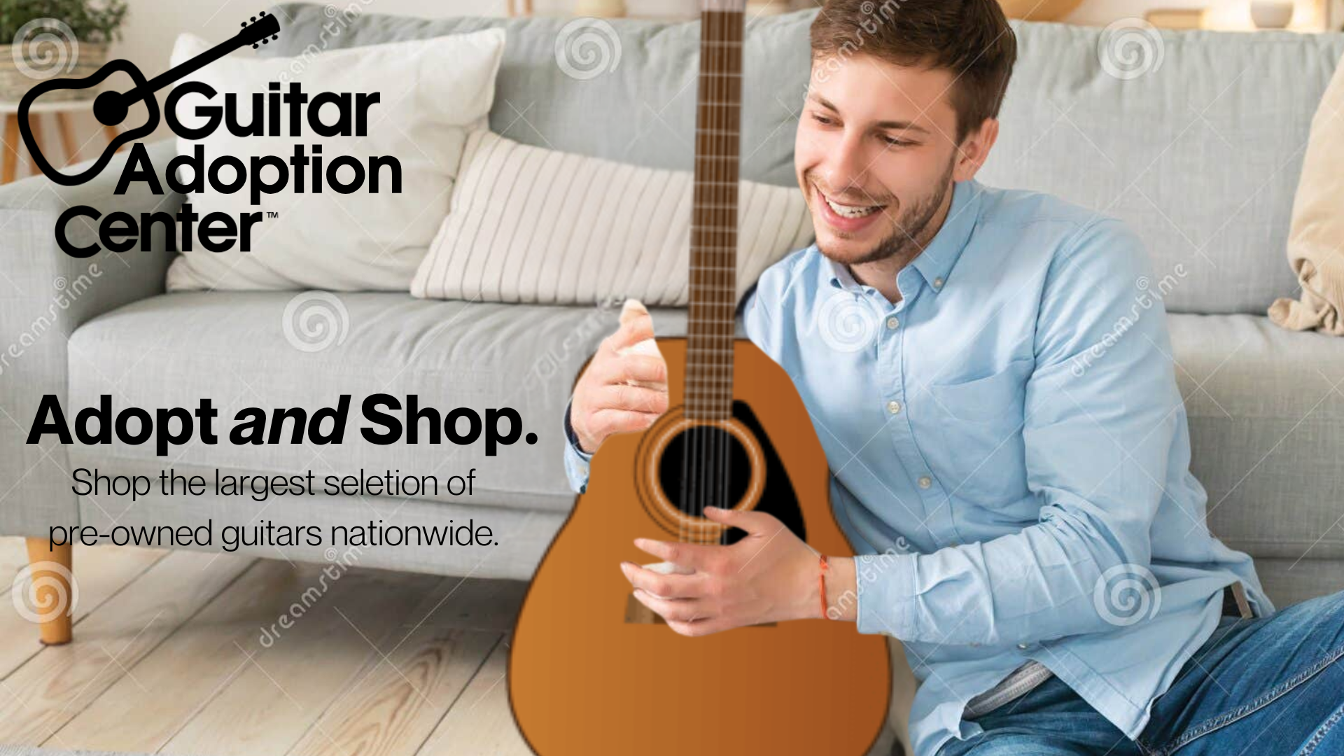 A young man sitting on a wooden floor, smiling and holding an acoustic guitar, in a cozy living room with a sofa and cushions behind him, promoting Guitar Adoption Center.