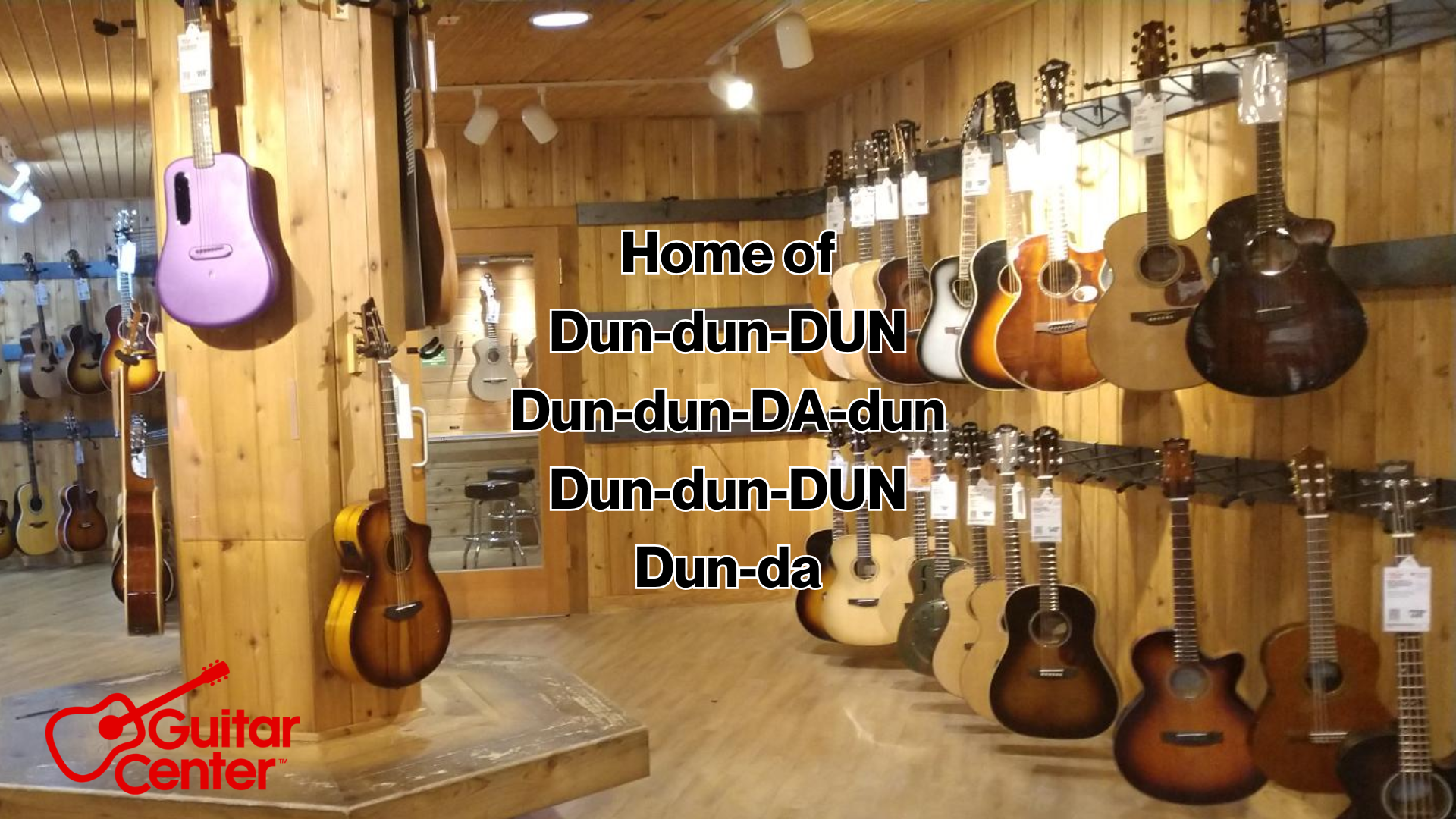 A guitar store display with various acoustic guitars hanging on wooden walls, and the text 'Home of Dun-dun-DUN Dun-dun-DA-dun Dun-dun-DUN Dun-da' overlaid on the image. The Guitar Center logo is visible in the bottom left corner.