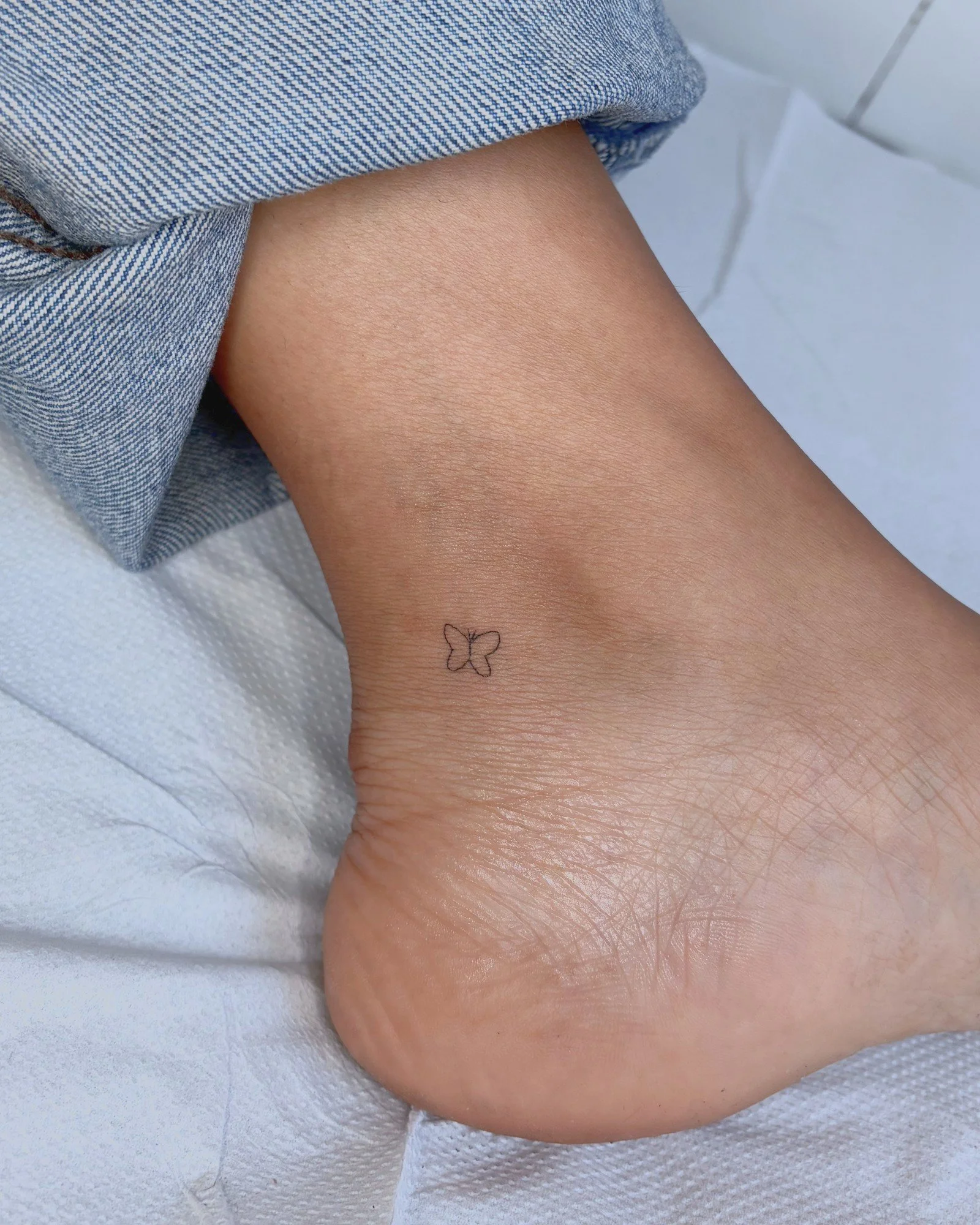 Tatouage fine line d'un petit papillon sur la cheville, réalisé par Finime à Lyon