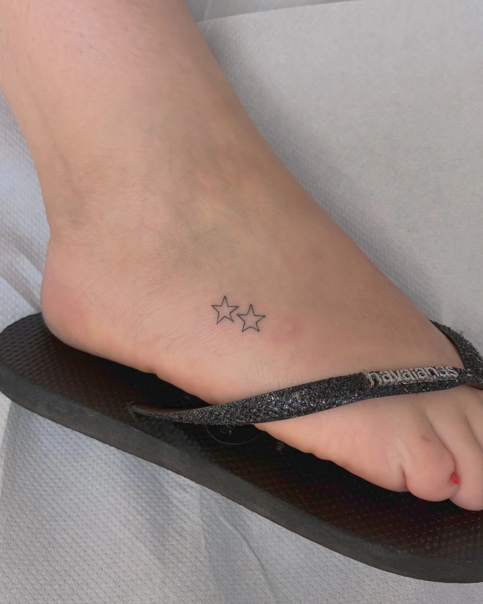 Tatouage fine line de deux petites étoiles sur le pied, réalisé par Finime à Lyon