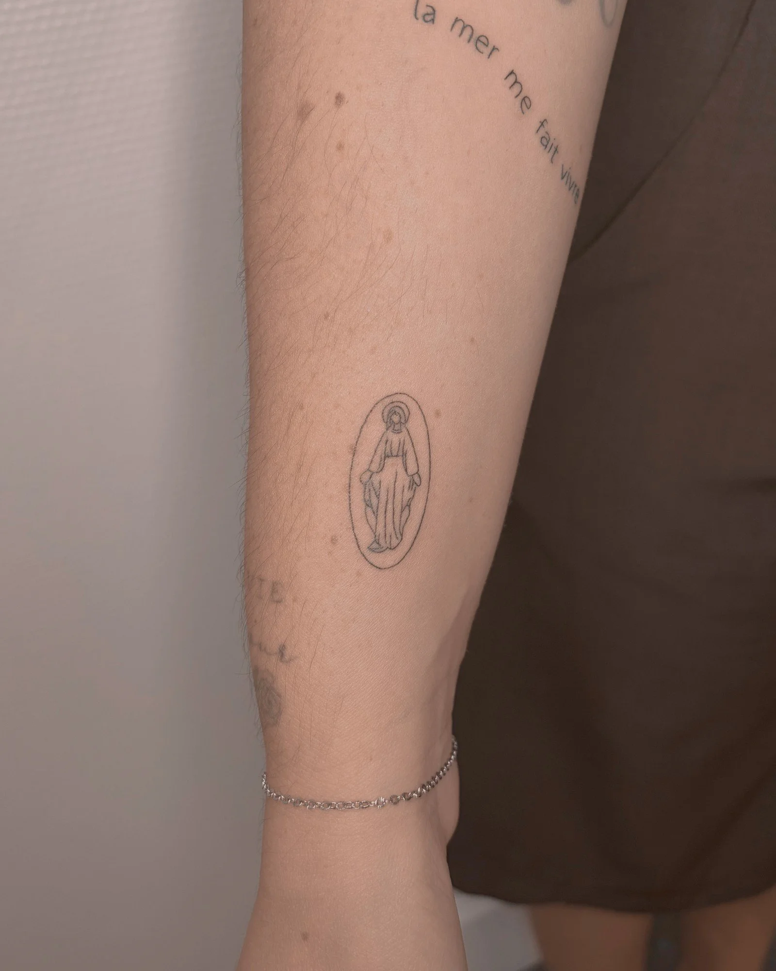 Tatouage fine line d'une médaille ovale sur l'avant-bras, réalisé par Finime à Lyon