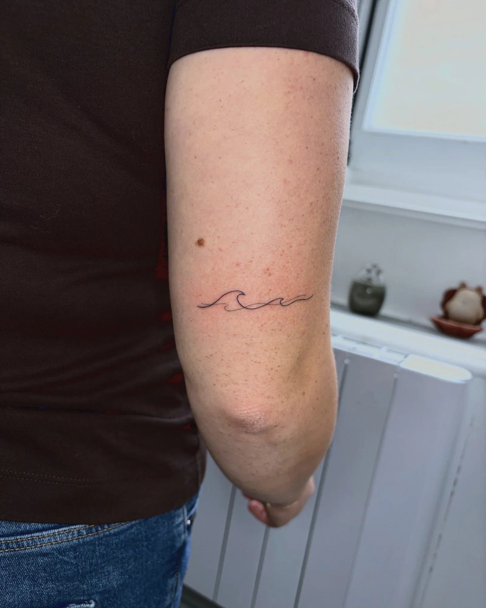 Tatouage fine line d'une petite vague sur le bras, réalisé par Finime à Lyon