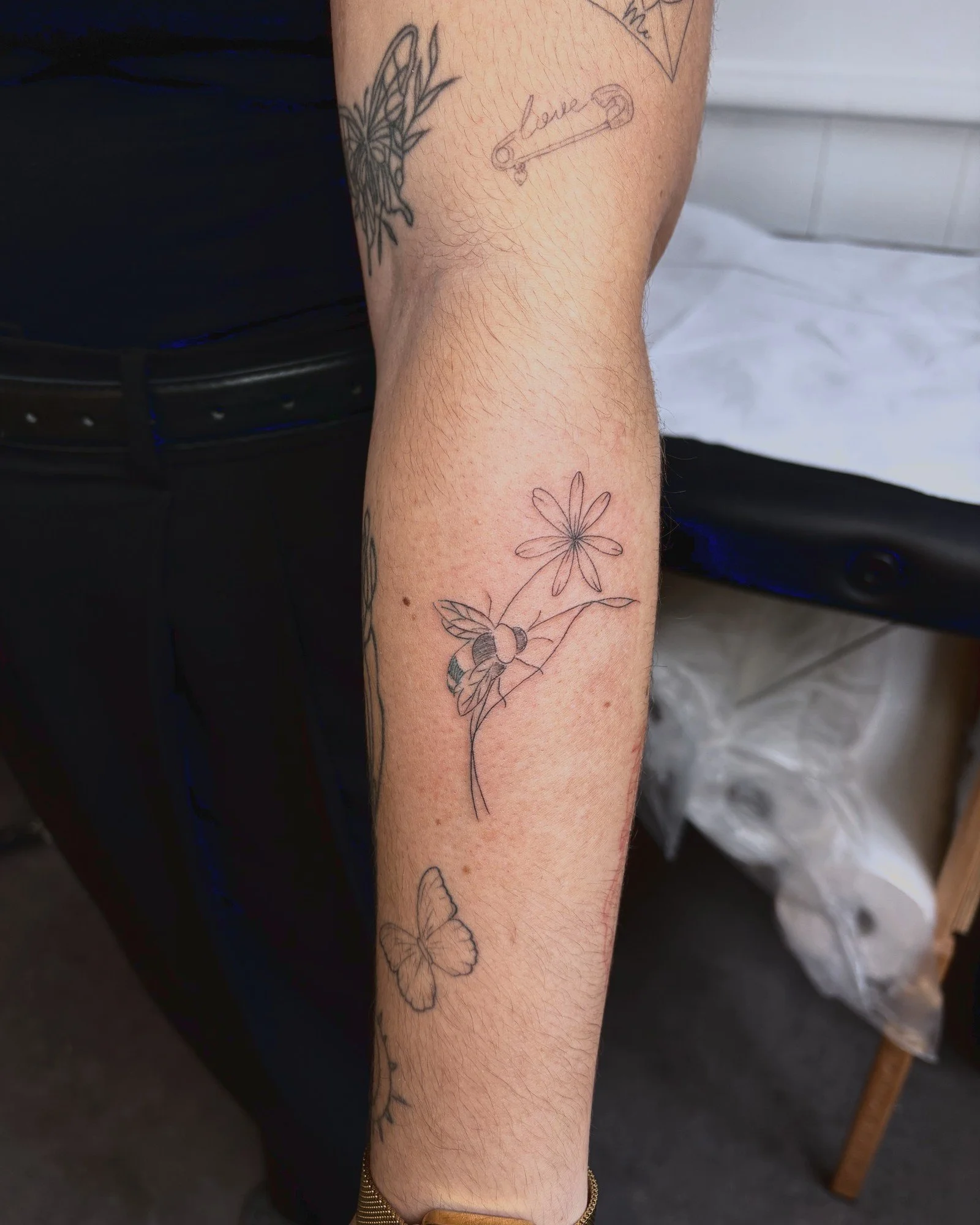 Tatouage fine line d'une fleur et d'un papillon sur l'avant-bras, réalisé par Finime à Lyon