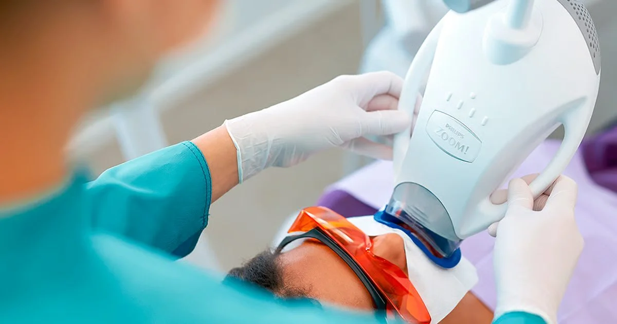 A medical professional performs a dental scan using a Philips Zoom! device on a patient lying down with protective glasses.