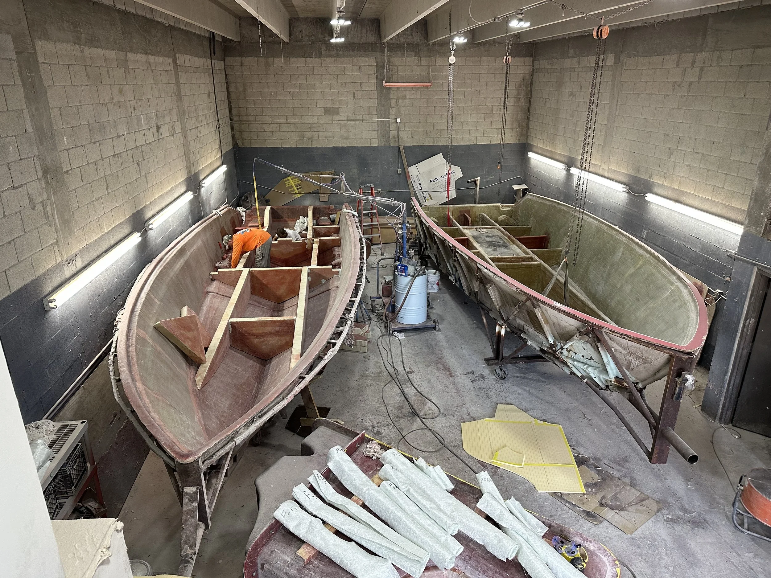 Two fiberglass boats under construction in an industrial workshop, Stringer Lamination: A close look at the fiberglass thickness, reinforcement, and clean finish of our laminated stringer system.