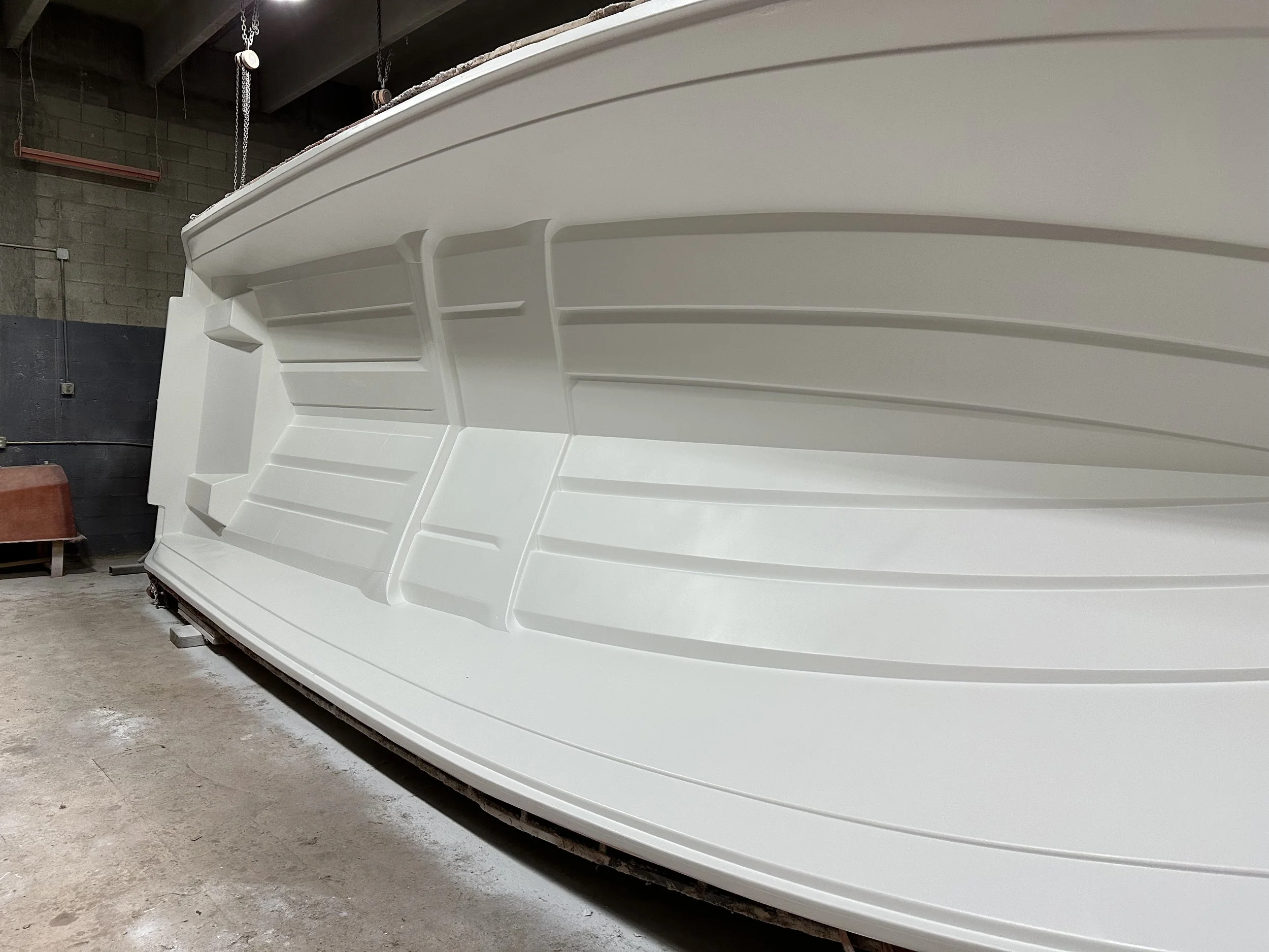 Large white fiberglass boat hull with molded Gelcoat Application: Fresh gelcoat applied inside the prepared mold, ready for the fiberglass lamination process to begin.