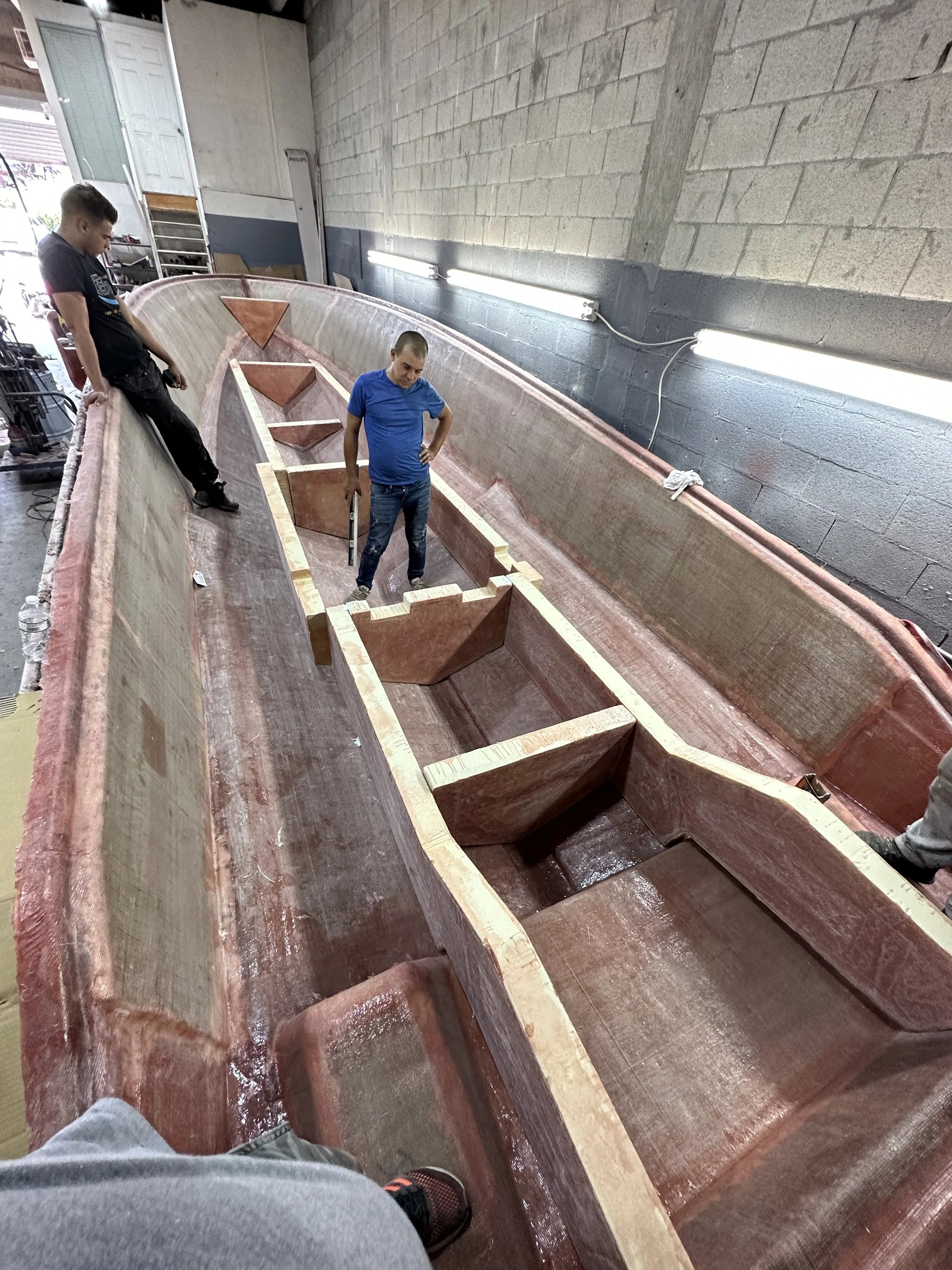 Two workers inspect the interior of a large fiberglass boat hull under construction in a workshop.Stringer Lamination: A close look at the fiberglass thickness, reinforcement, and clean finish of our laminated stringer system.