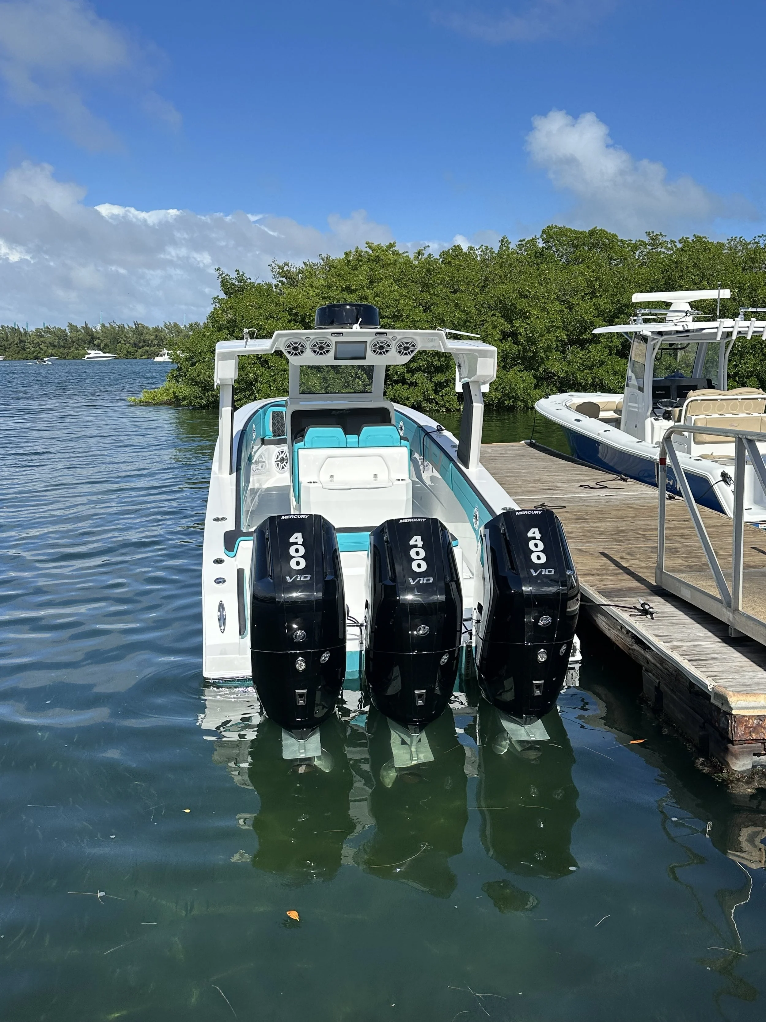 Large center-console powerboat with three Mercury 400 V10 outboard engines docked beside another boat on calm tropical water.