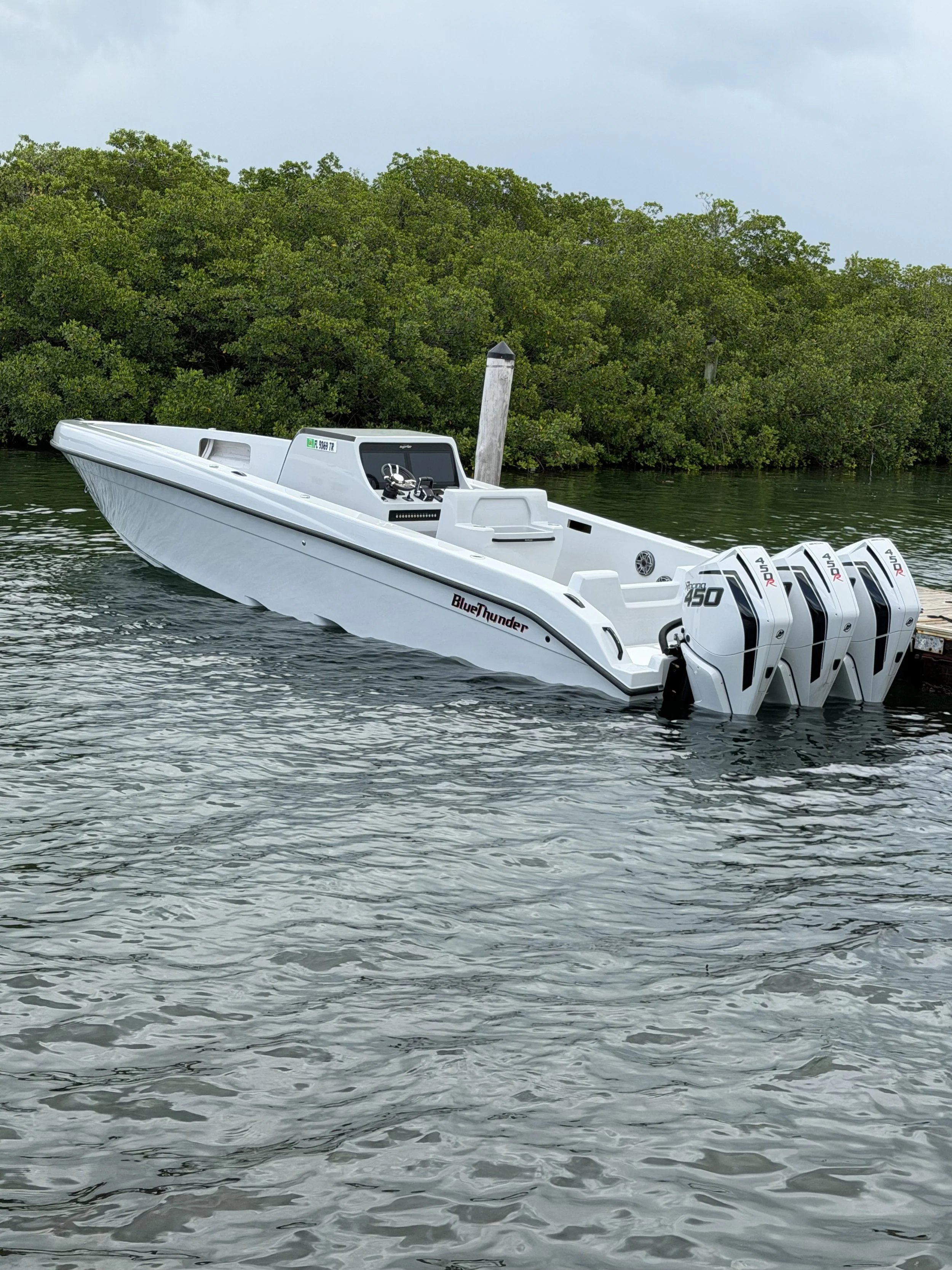 White BlueThunder speedboat with four outboard motors cruising on calm water beside a mangrove shoreline