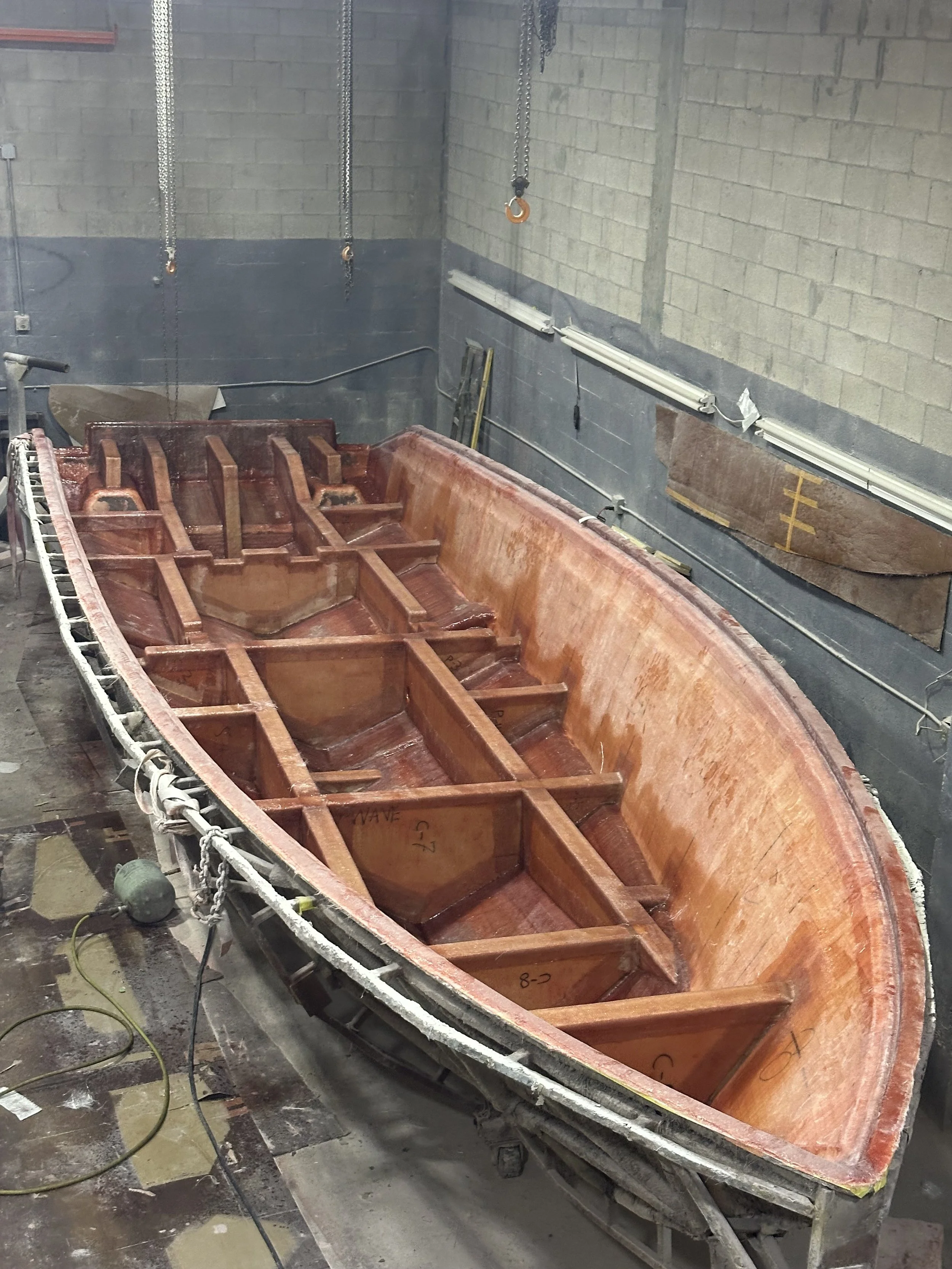 Large fiberglass boat hull under repair in an industrial workshop, Stringer Lamination: A close look at the fiberglass thickness, reinforcement, and clean finish of our laminated stringer system.