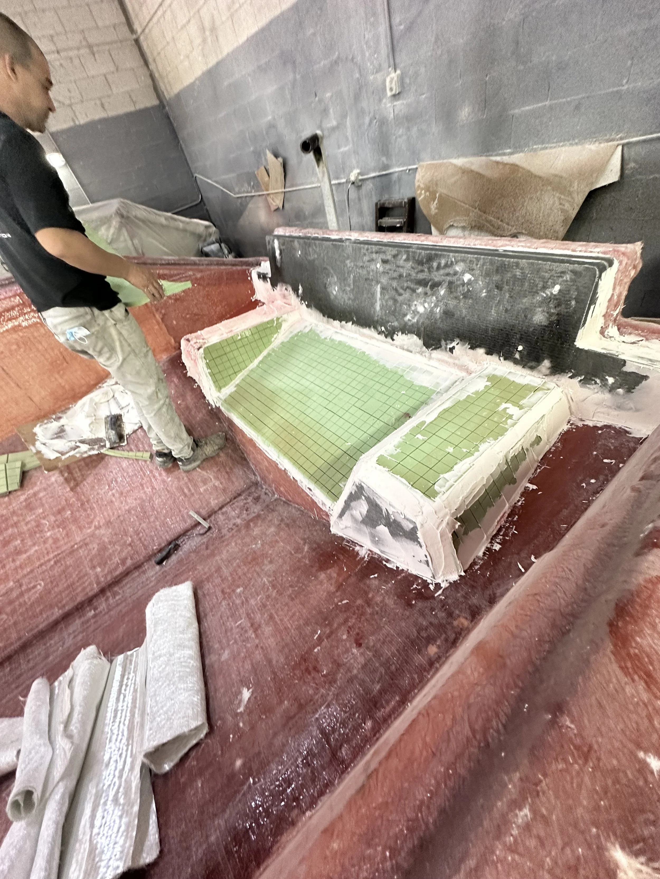 Resin Application: Resin is worked through the fiberglass fabric with attention to consistent saturation throughout the laminate.

Laminate Consolidation: Each fiberglass layer is carefully rolled to remove trapped air and bring the layers into close