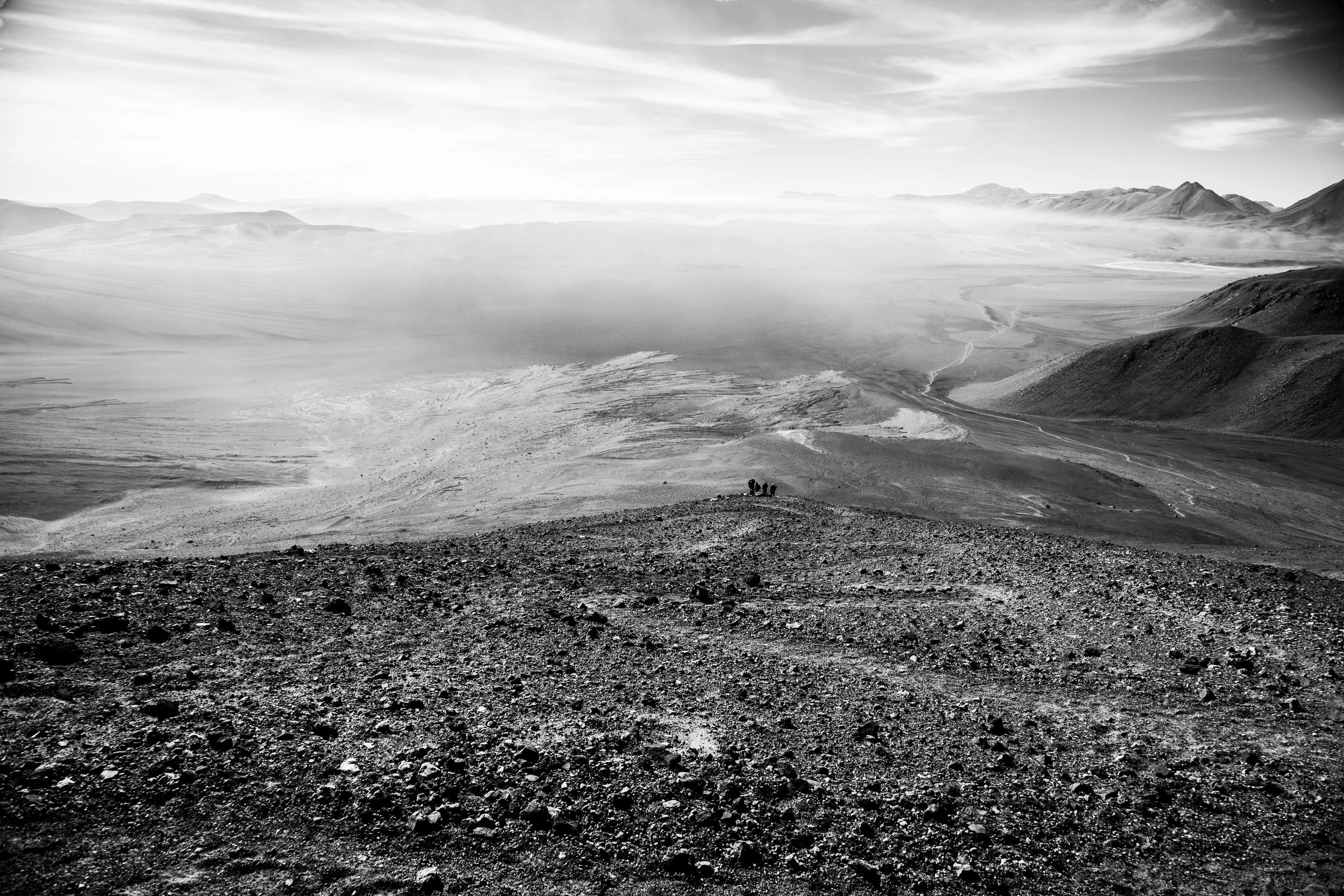 Black and white landscape photo of a desert with mountains in the distance and a vast sky with clouds.