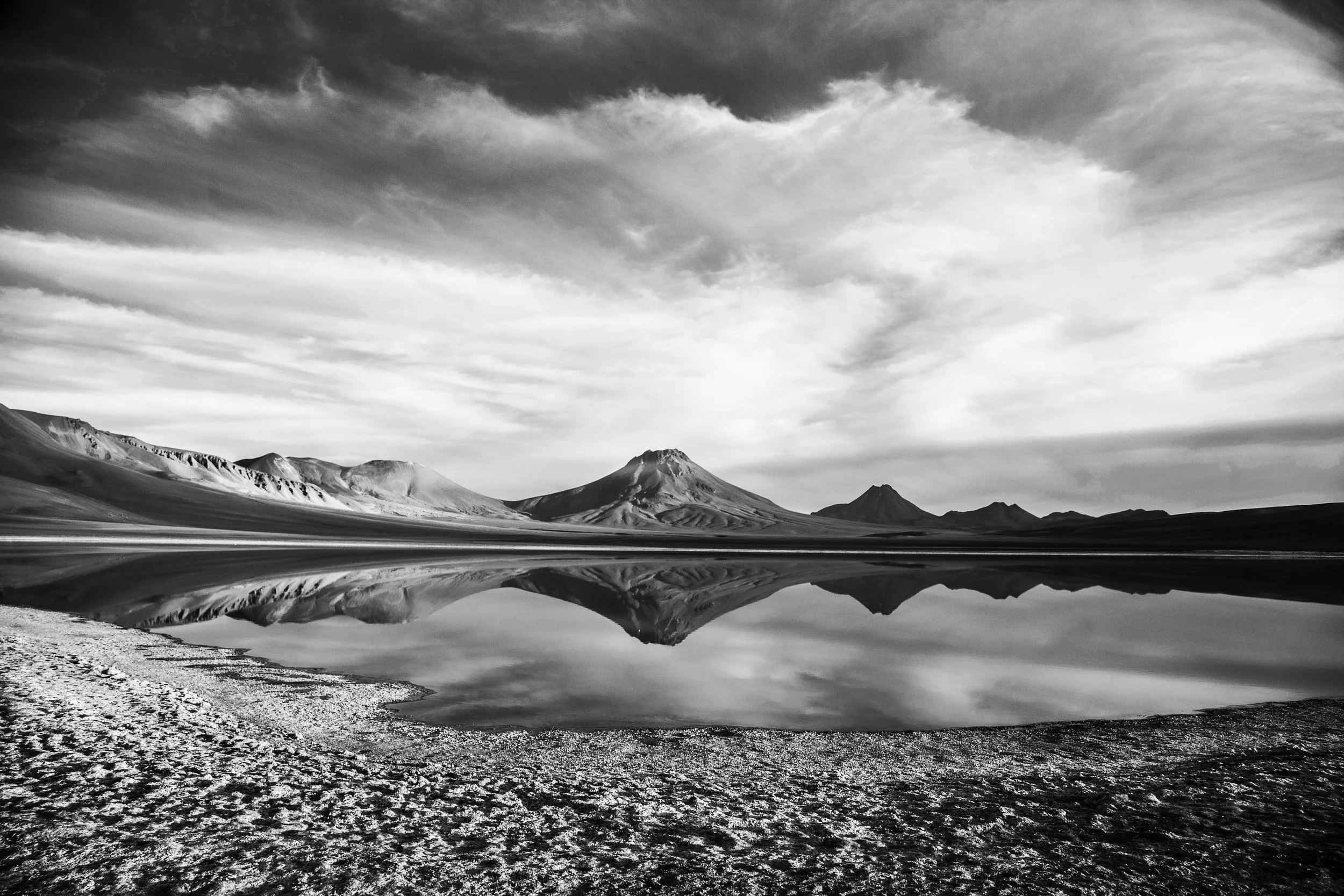 Black and white landscape of mountains, a lake with reflections, and a cloudy sky.