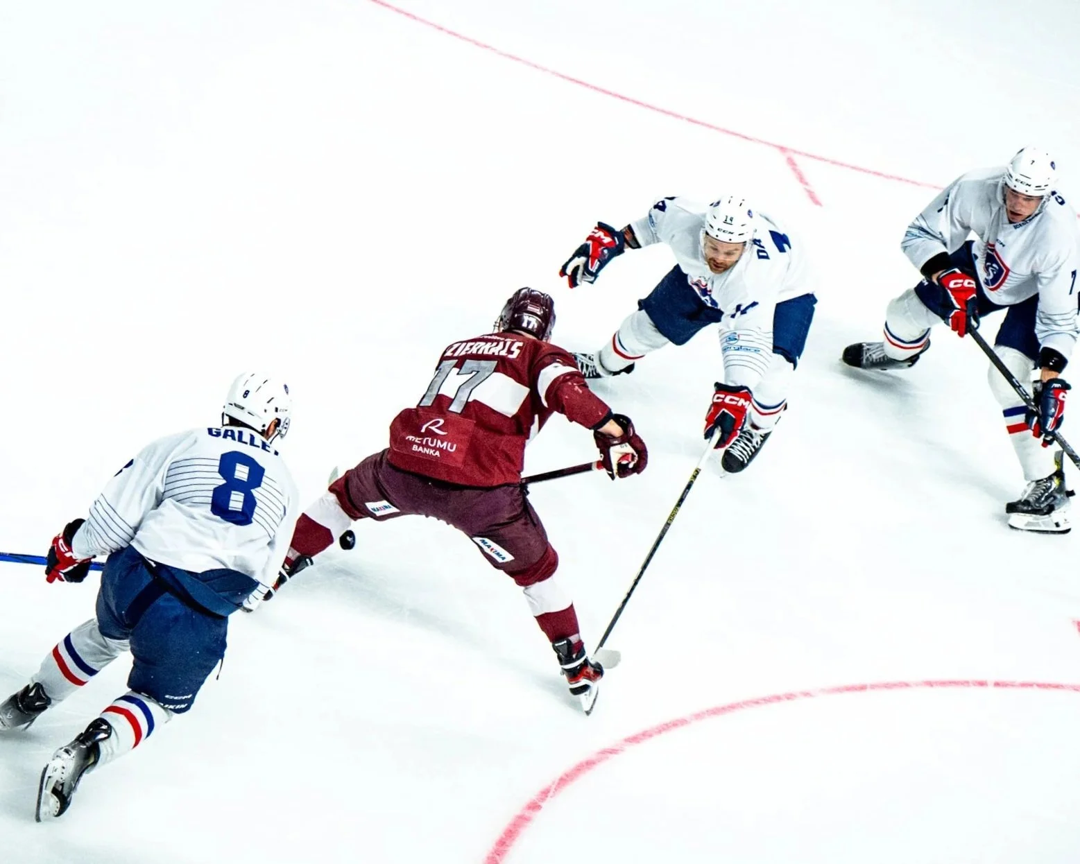 TEAM LATVIA Hockey players in action during a game, with three players in white jerseys and one in a maroon jersey fighting for the puck.
