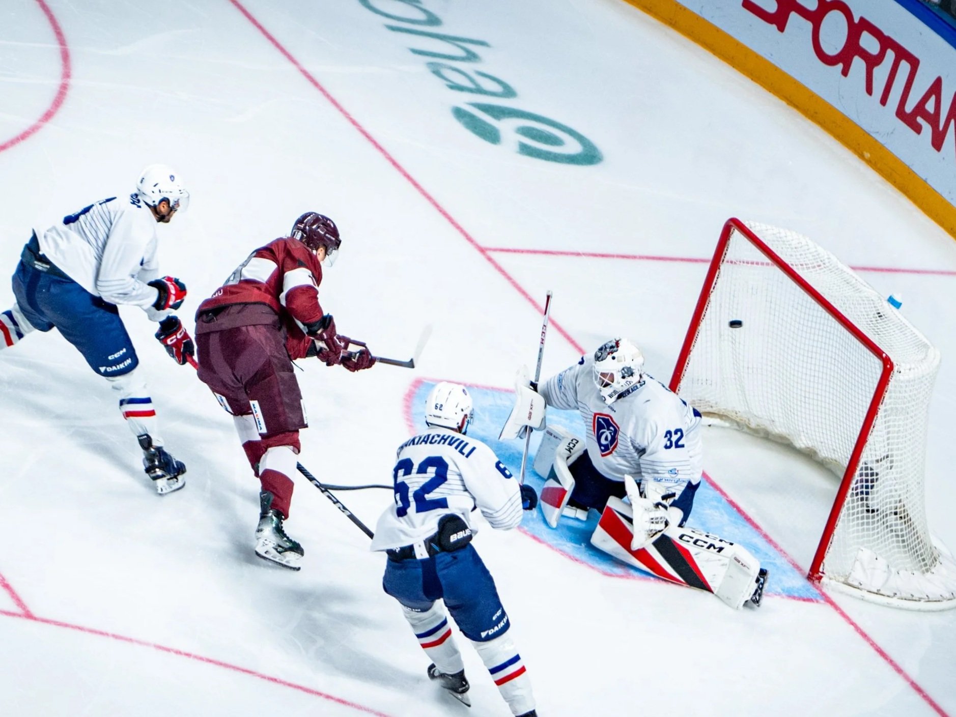 Ice hockey players competing for puck in front of goal during game.