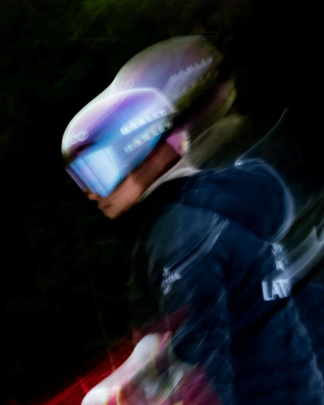 This is a blurry, motion-affected photo of a person holding a smartphone at night, with the bright screen and hand visible, but the rest of the scene is indistinct due to motion blur.