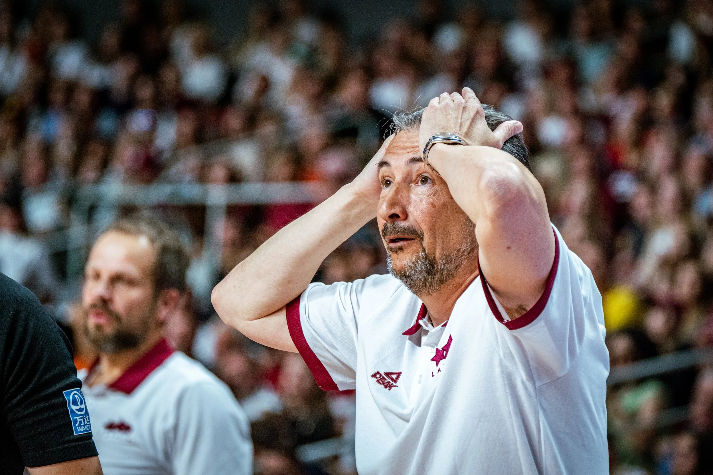 luca banchi with his hands on his head during a sporting event, surrounded by other fans in the background.