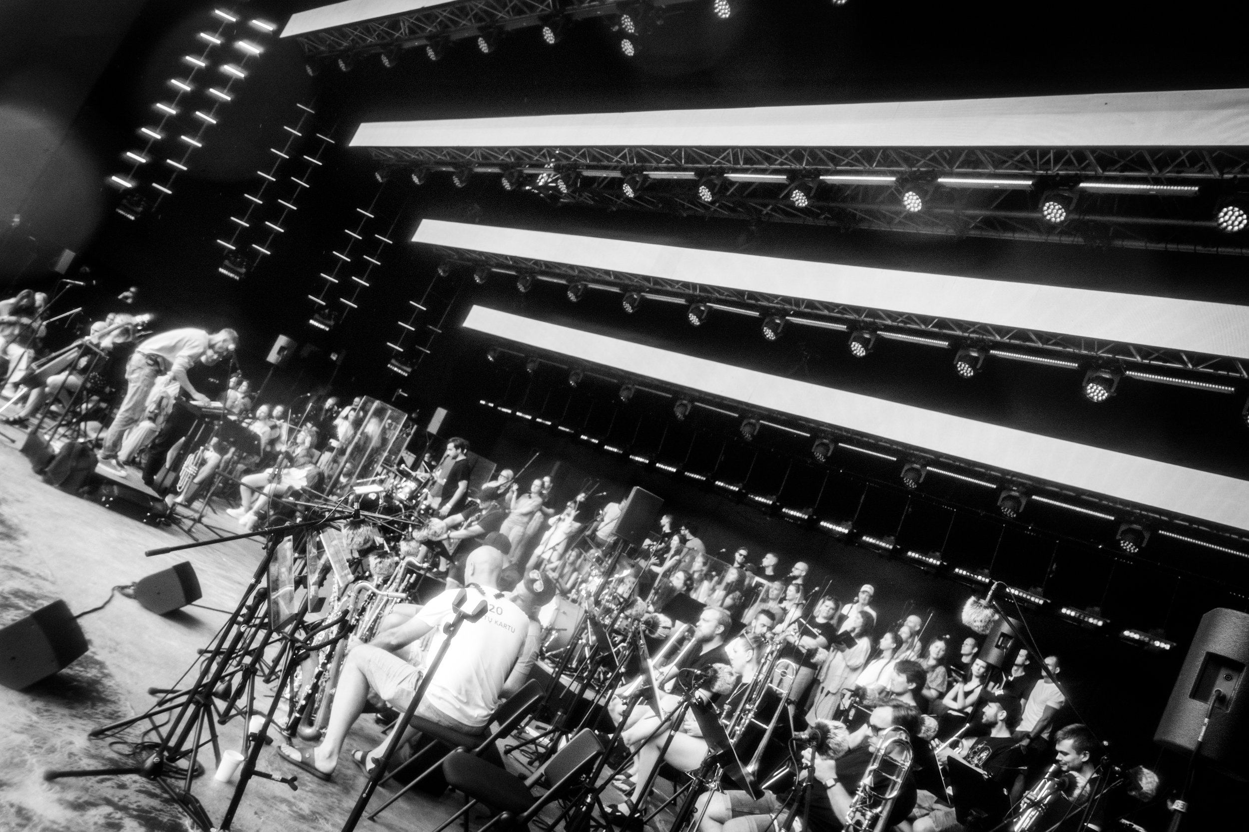 A large group of musicians and singers performing on a stage with extensive lighting and large screens above them.