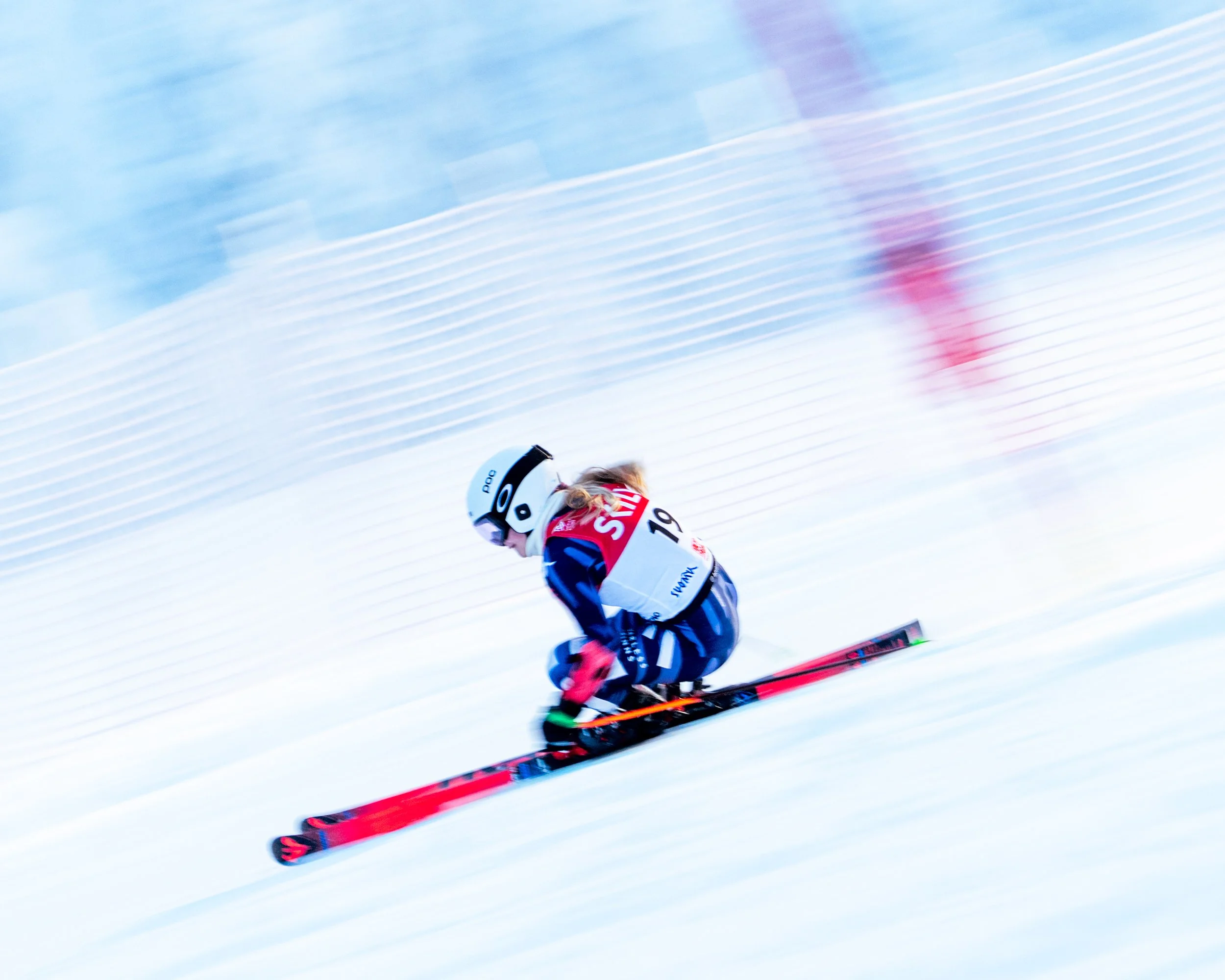 A skier in a red, white, and blue outfit racing downhill on snow, wearing a helmet with the number 19 on it.