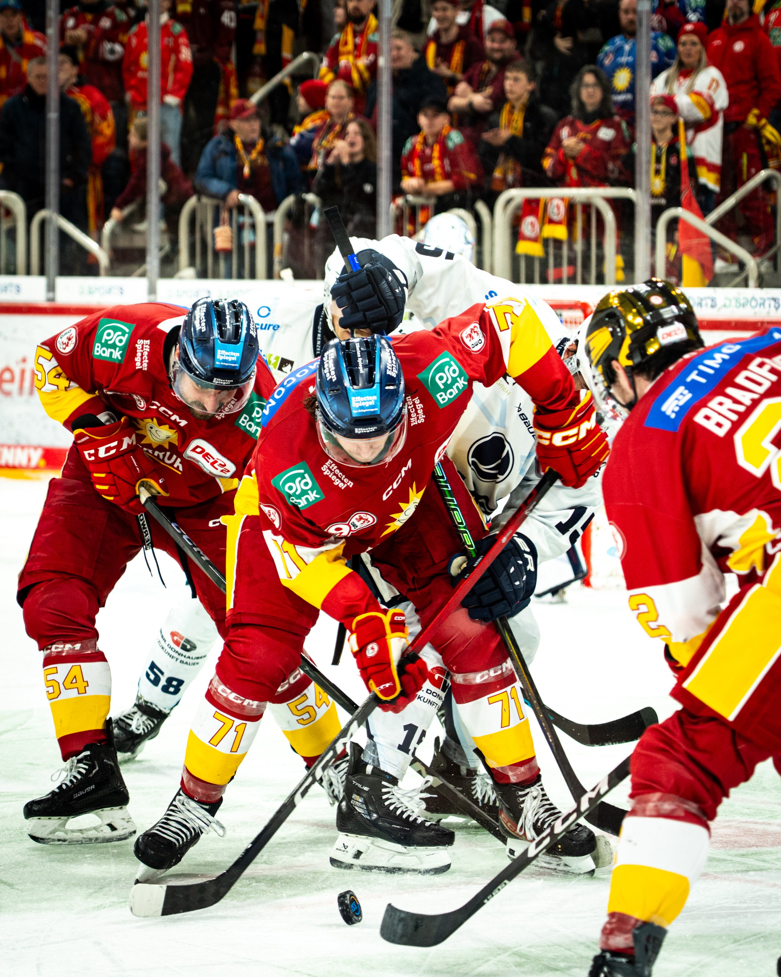 Düsseldorfer EG. Hockey players in red, yellow, and white jerseys compete on an ice rink while spectators watch behind the glass.