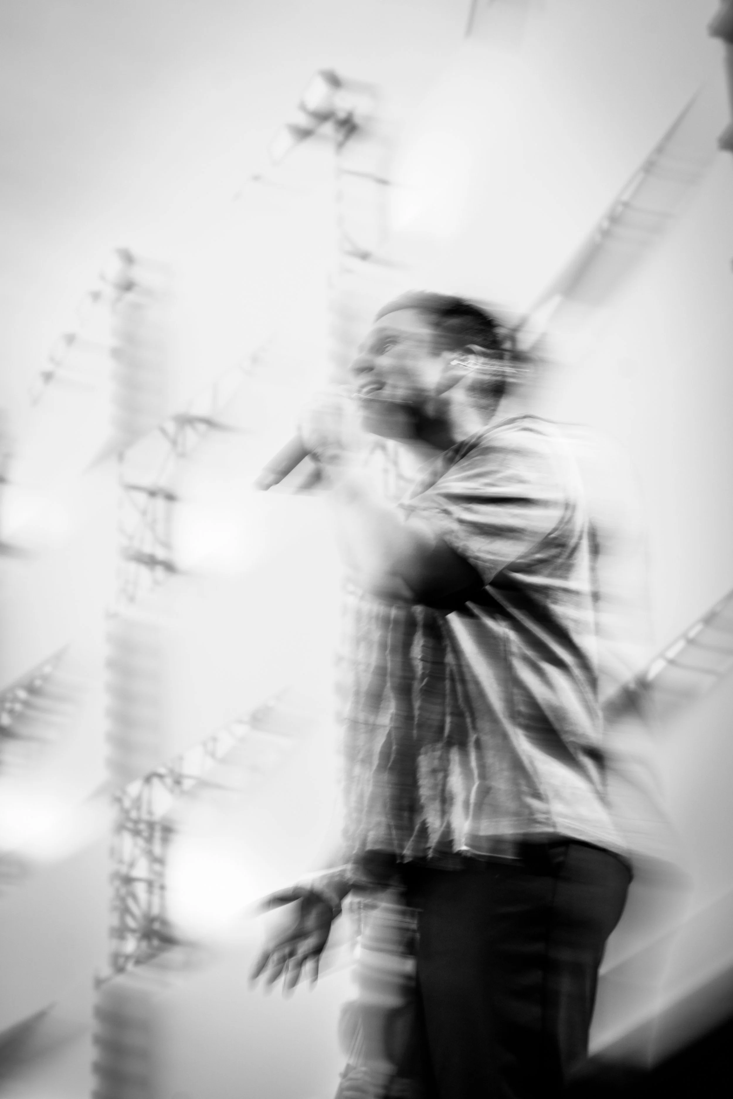 Blurred black and white photo of a person standing near a wall with decorative elements, arms raised, and hair tied back.