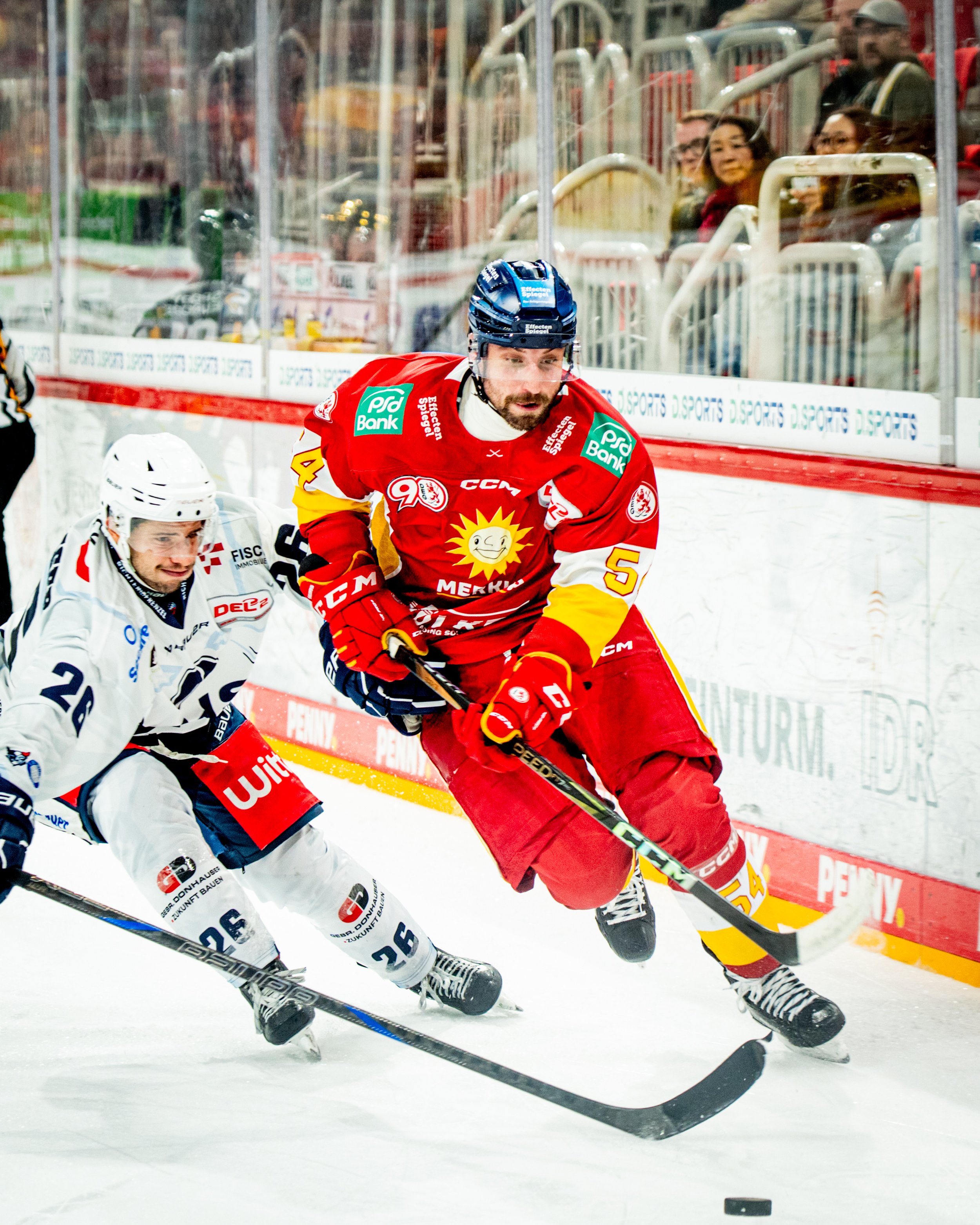 Hockey players in action during a game with players from opposing teams competing for puck control near the boards.