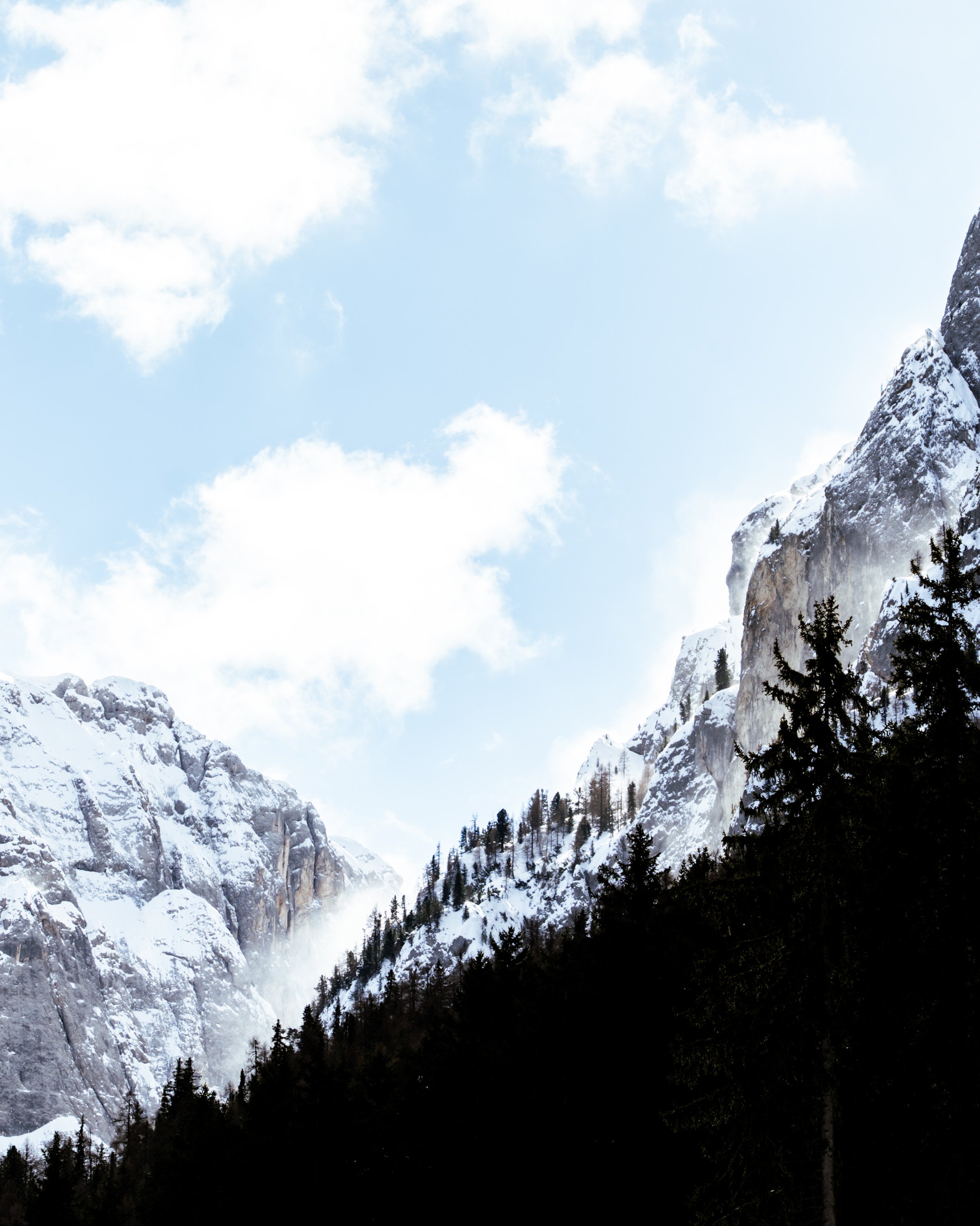 Snow-covered mountain landscape with a waterfall, evergreen trees, and a cloudy sky.