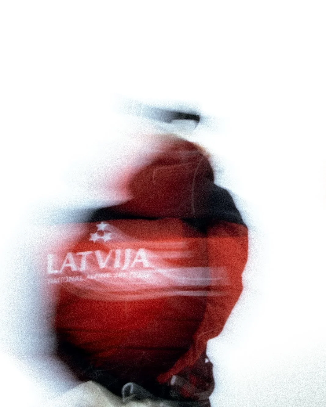 Blurred image of a red bag with white text and a white star, with a person wearing a black jacket and a red hoodie behind it.