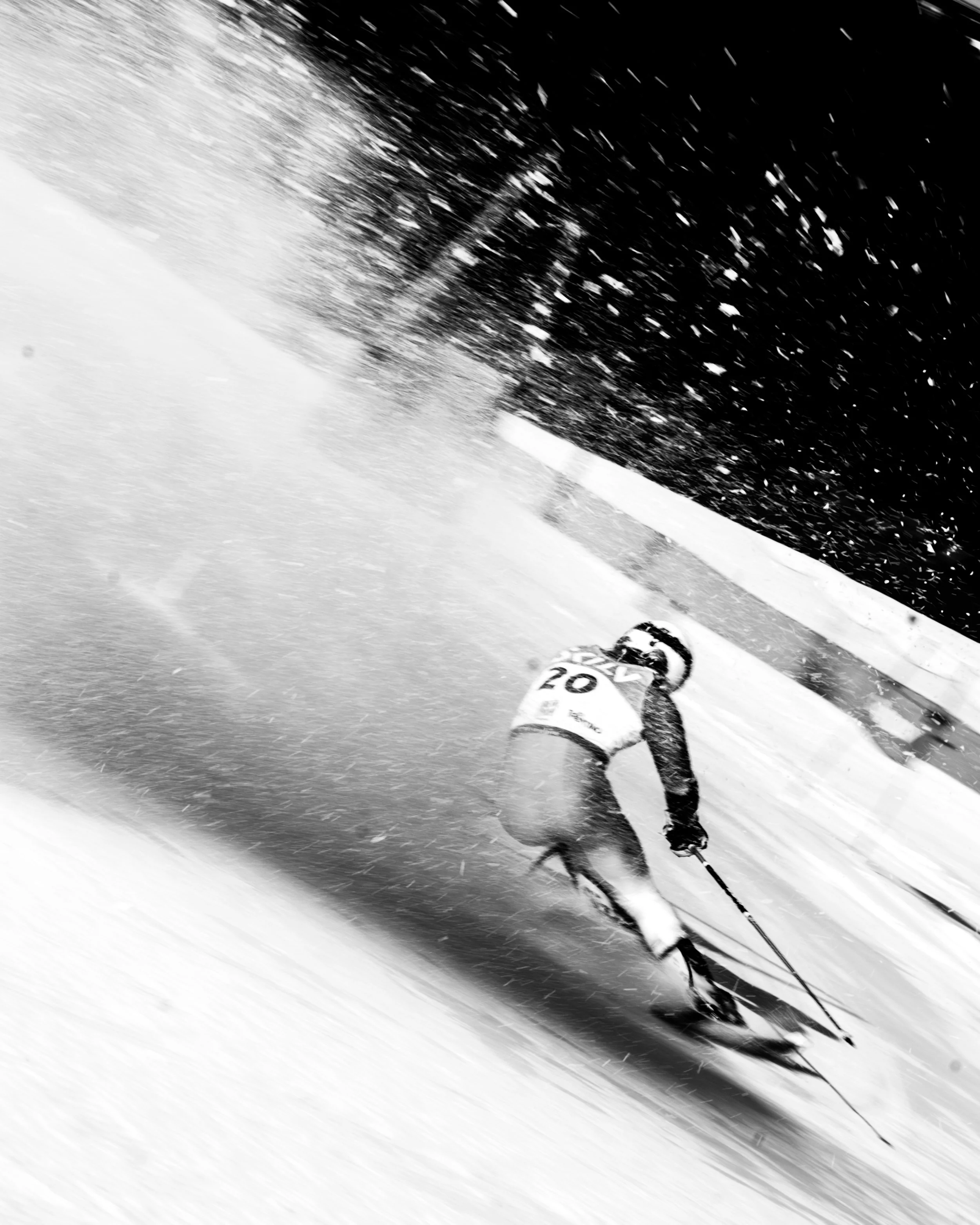 A skier in a racing suit with the number 20 on it is skiing downhill in a snow-covered slope during a competitive skiing event at night.