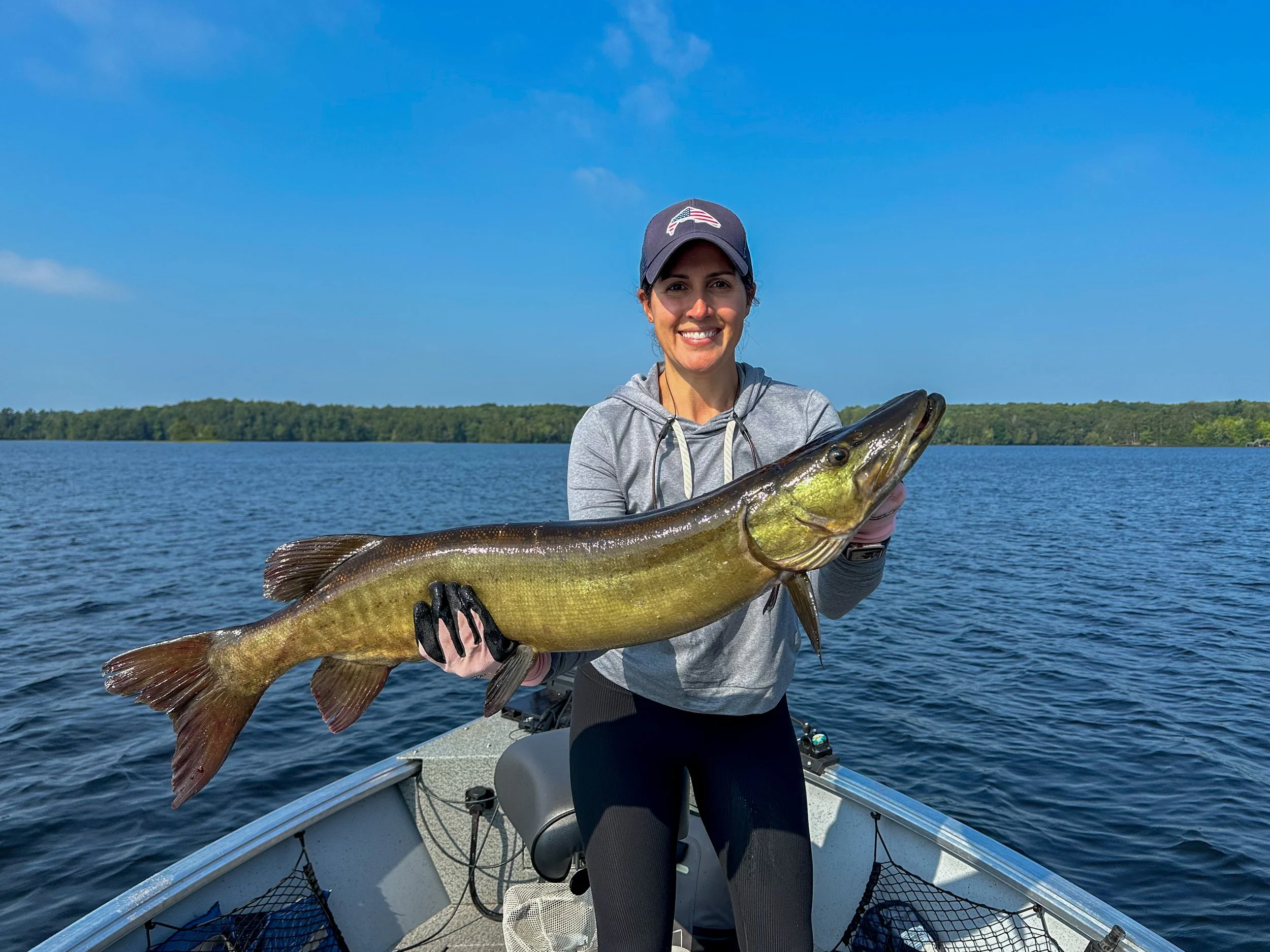 Woman holding a large northern pike on a fishing boat in a lake