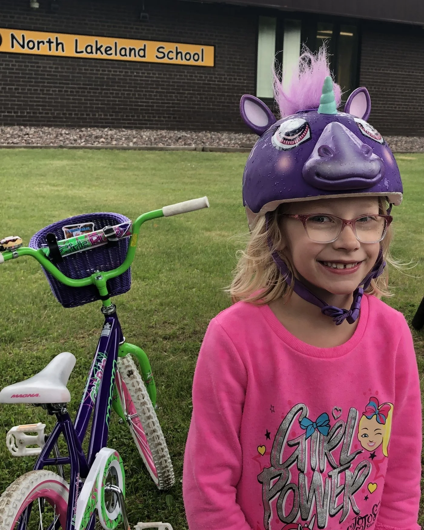 Smiling girl wearing a purple unicorn helmet beside her colorful bicycle outside North Lakeland School