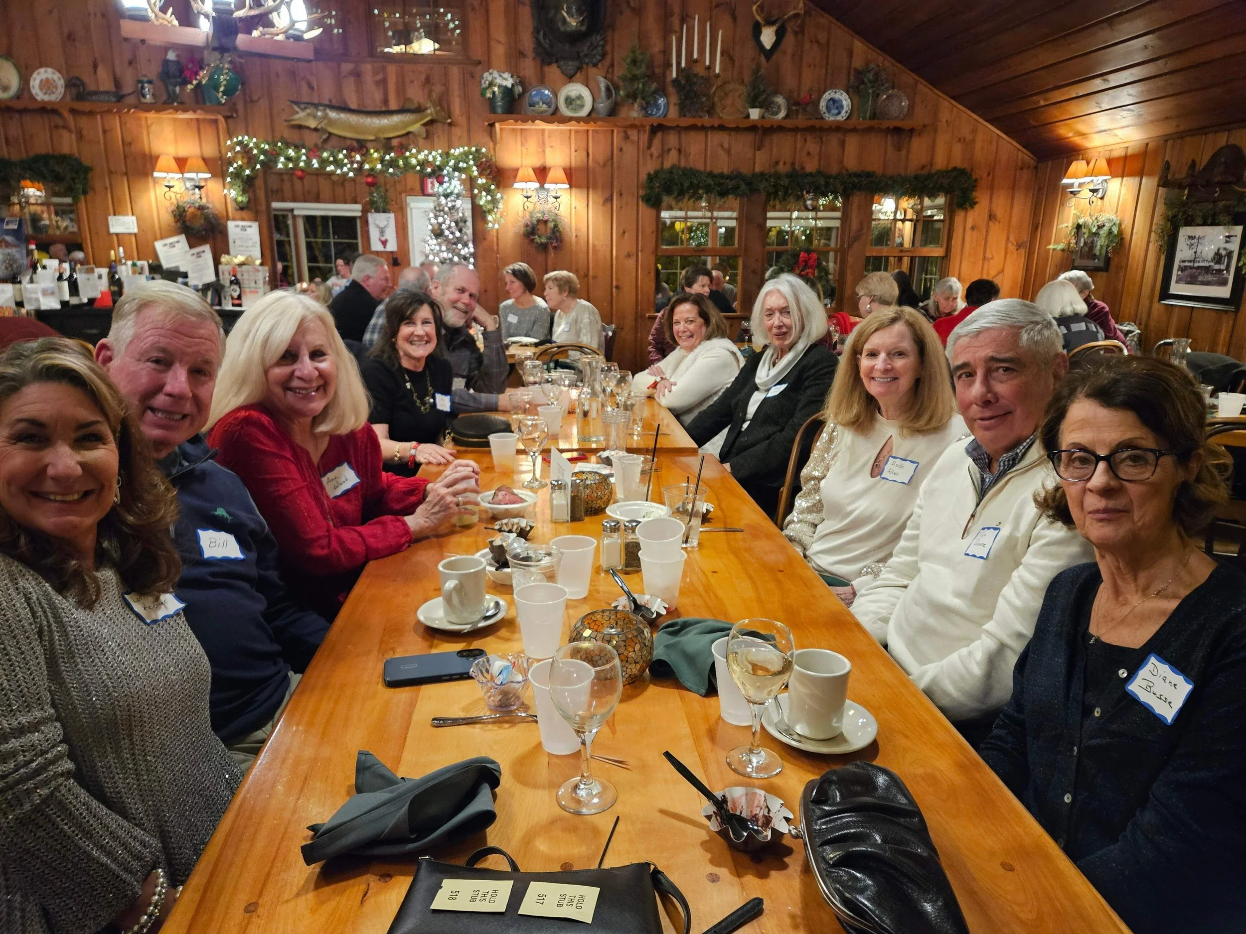 Large group dining together at a festive wood-paneled restaurant decorated with holiday garlands and mounted wildlife.