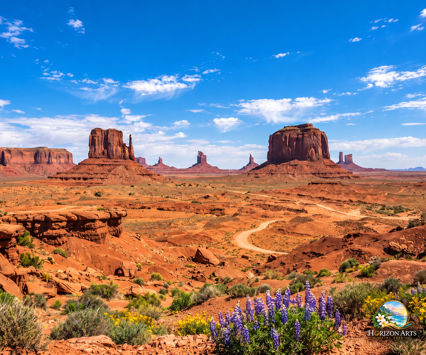 Panoramic Monument Valley desert landscape with red sandstone buttes, winding dirt road, wildflowers, and blue sky