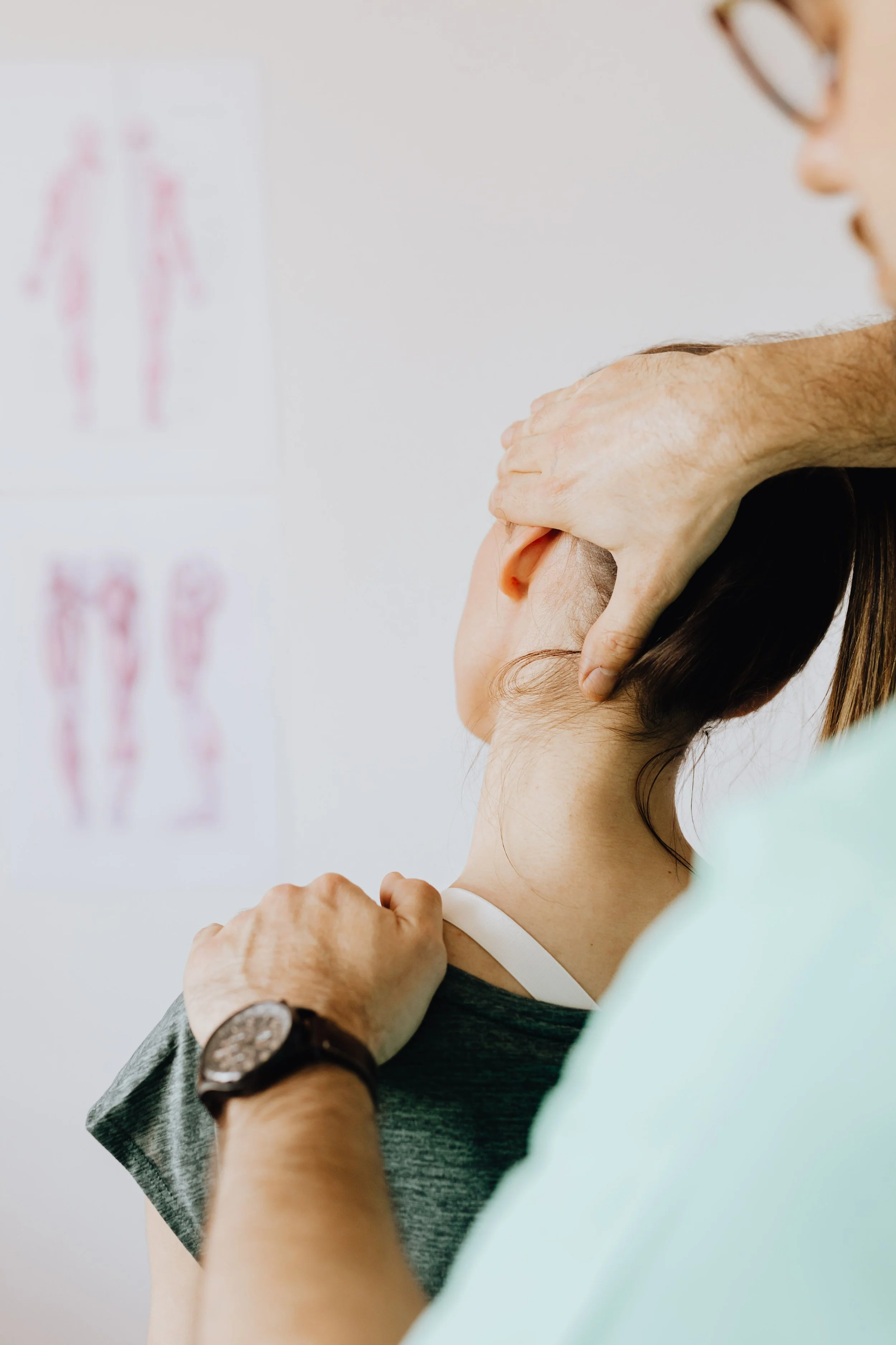 A chiropractor stretching a young woman's neck and shoulder area in a clinical setting.