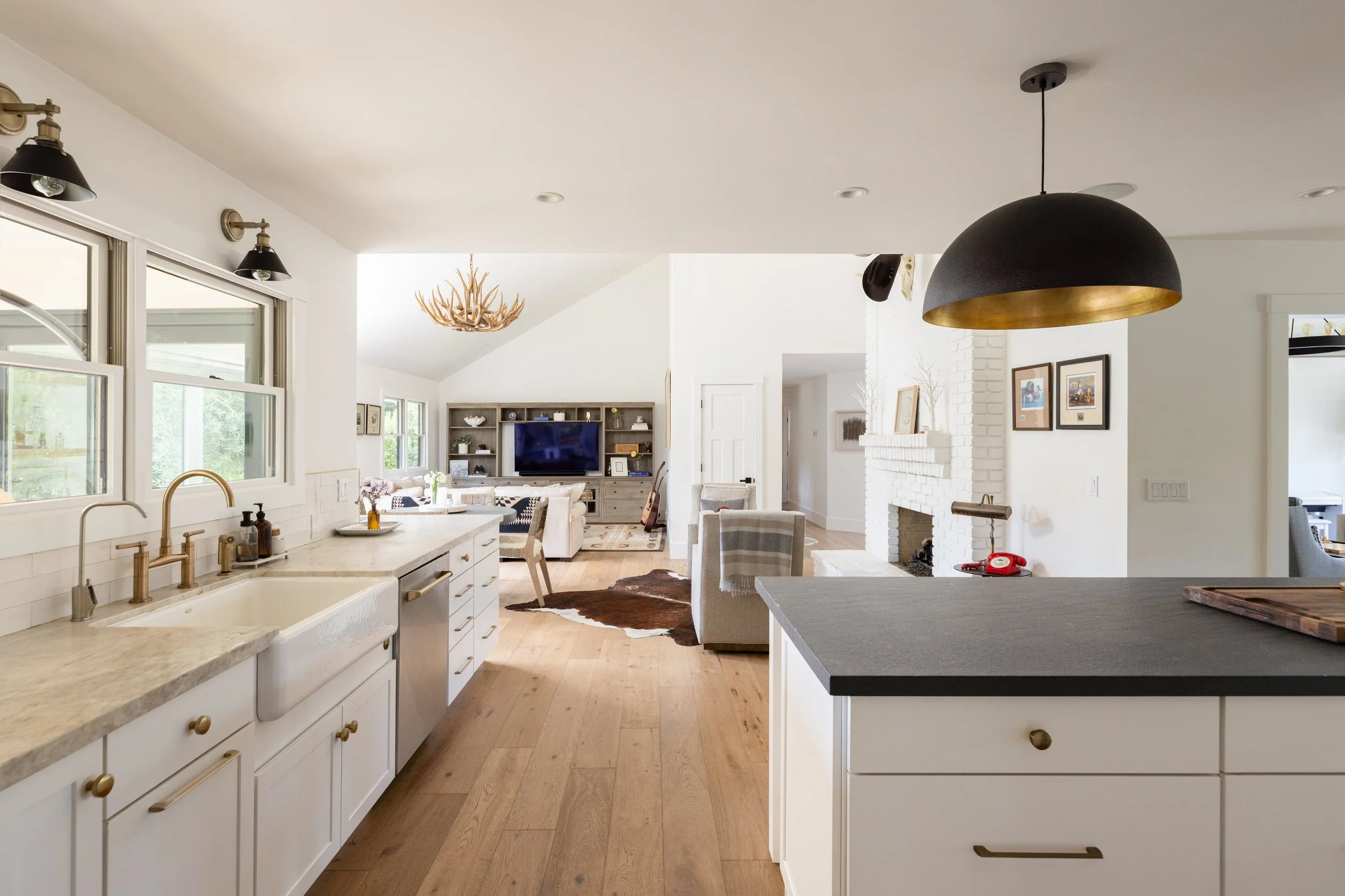 Open-concept kitchen and living room with white cabinets, black and gold pendant light, and wooden floor.