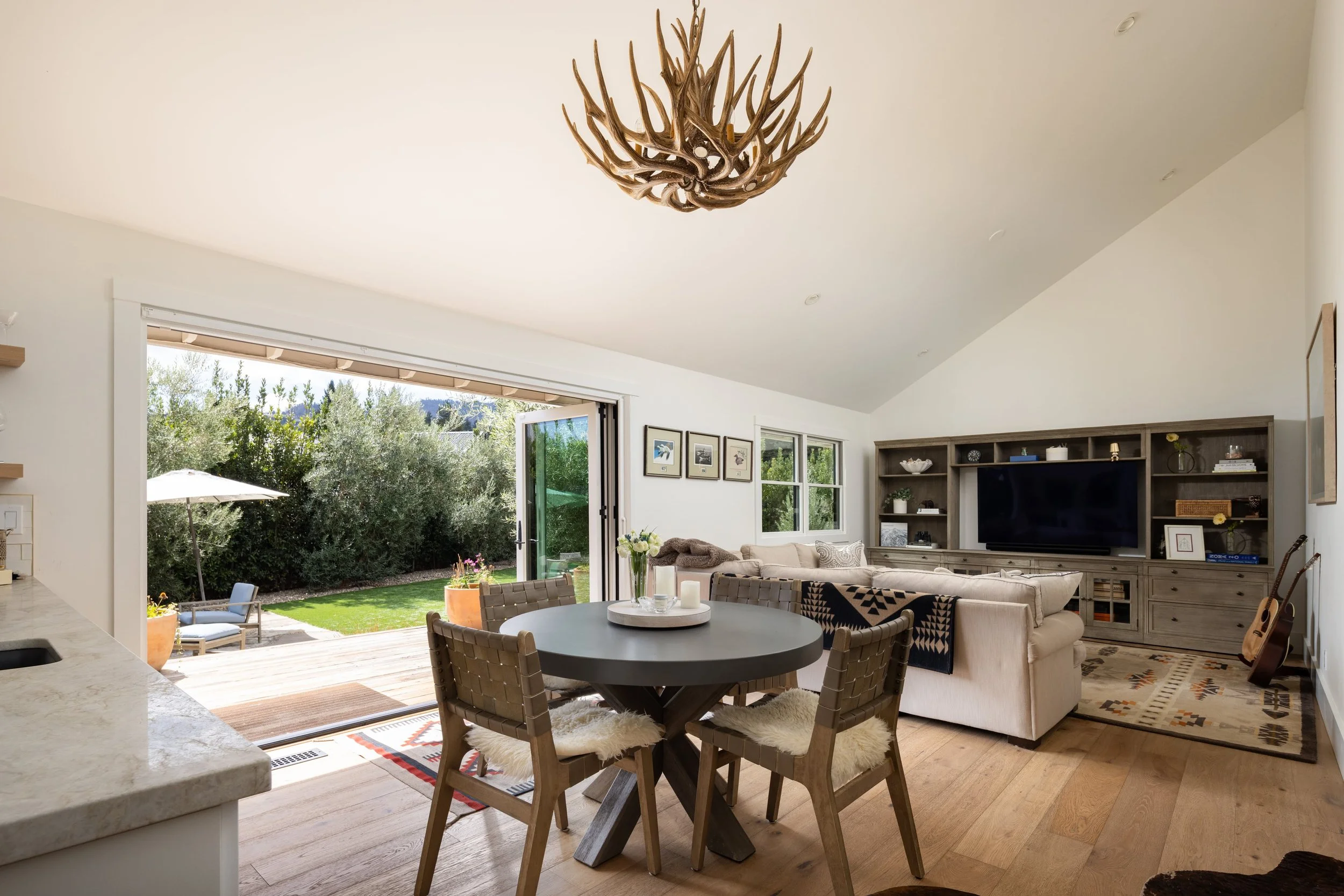 Living room with open glass door leading to backyard, featuring seating area, television, wall art, and wood floors.