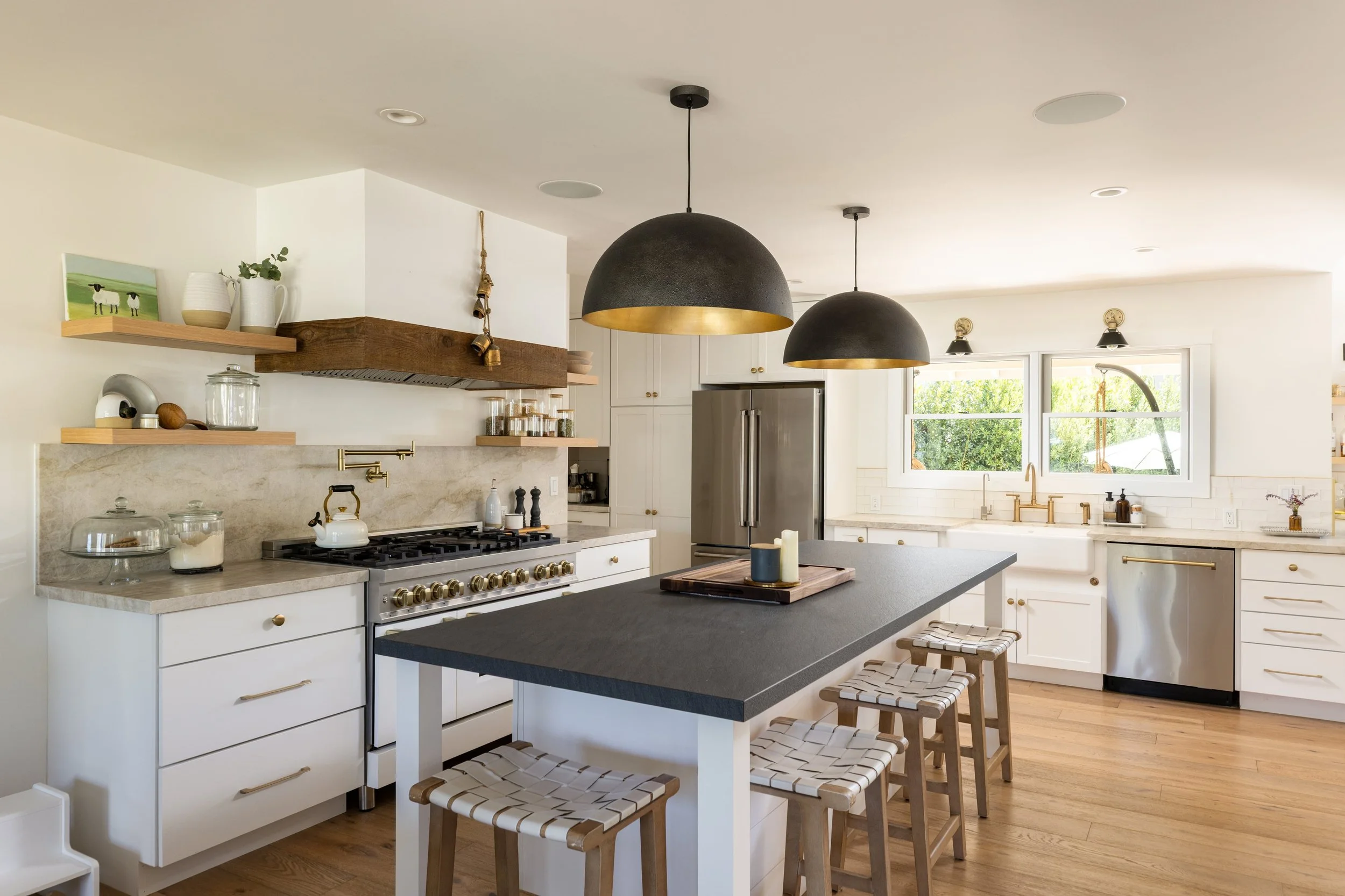 Modern kitchen with white cabinets, black countertops, wooden bar stools, and black and gold pendant lights over a kitchen island.