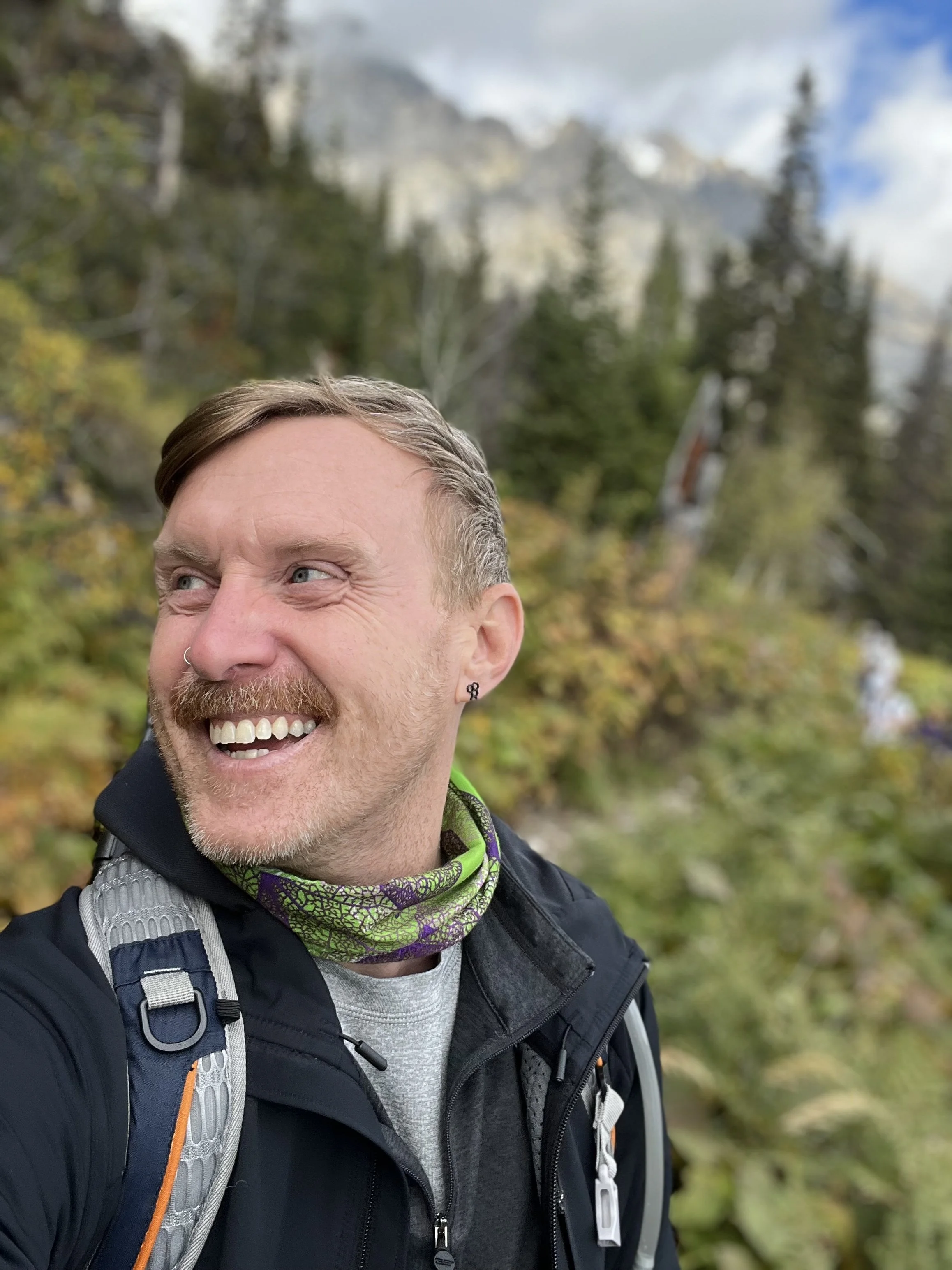 Joshua Beeson, Baltimore-based independent travel advisor, smiling on a mountain hike